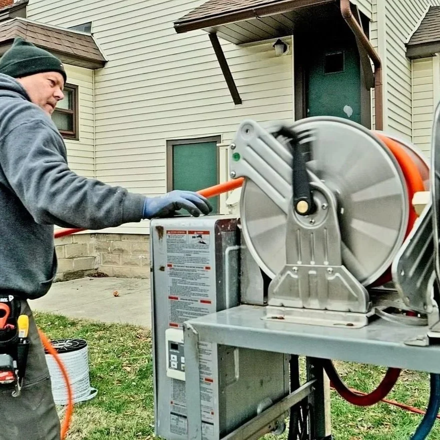 Technician operates a hydro jetting machine during a residential sewer cleaning service, illustrating the equipment used to clear grease, roots, and buildup from drain lines with high-pressure water.
