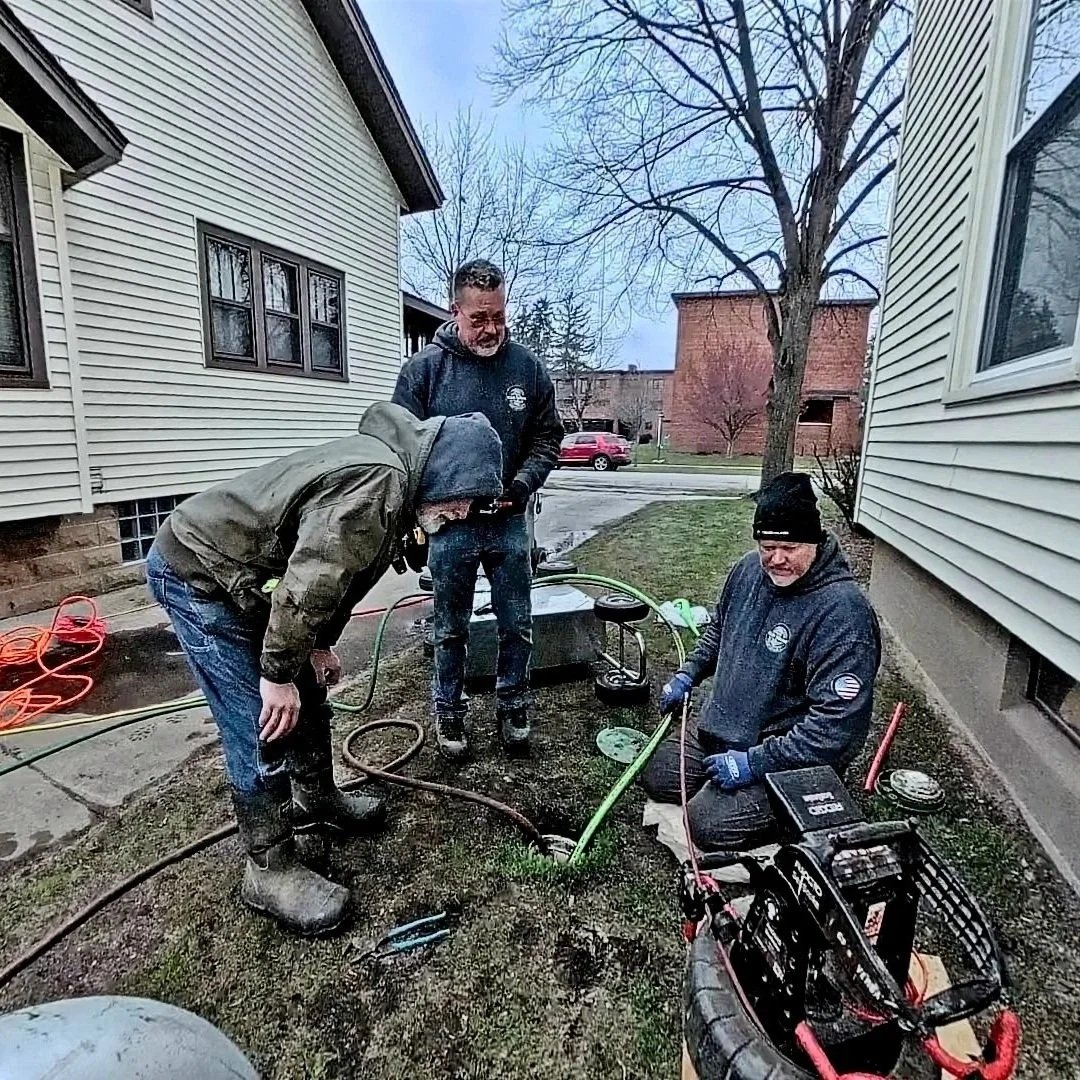 Technicians hydro jetting residential main sewer line outdoors, clearing grease sludge and buildup to restore full pipe flow capacity.