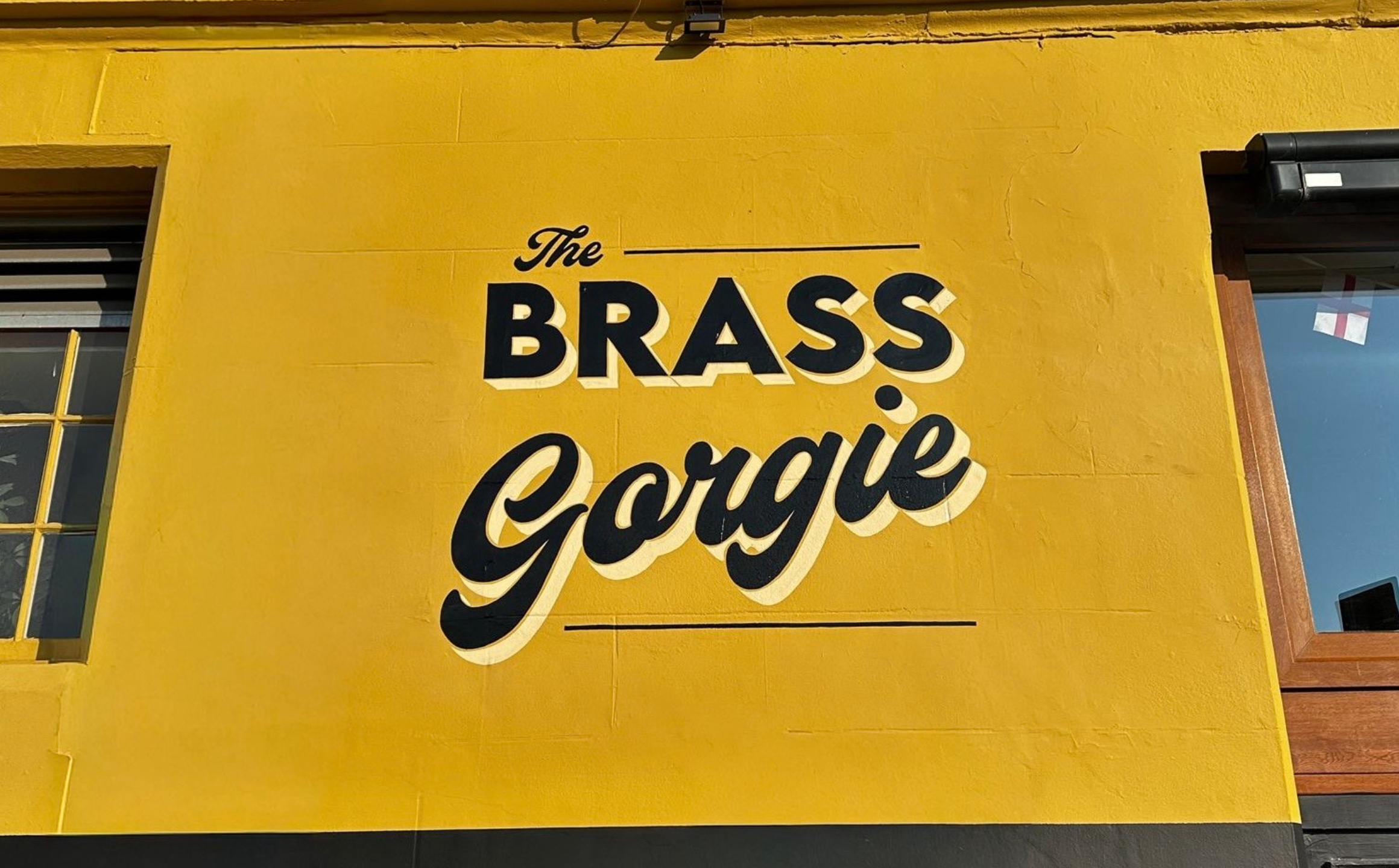Yellow exterior wall of a building with a sign that reads 'The Brass Goose' in black and white lettering.