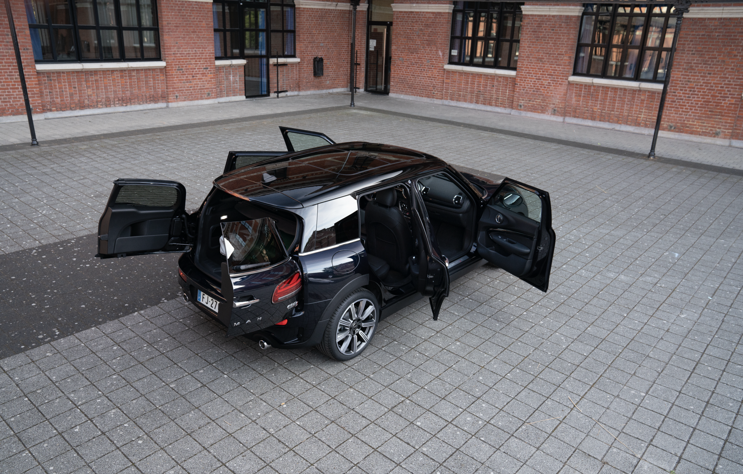Voiture noire électrique avec portes ouvertes, stationnée sur une place pavée devant un bâtiment en brique.