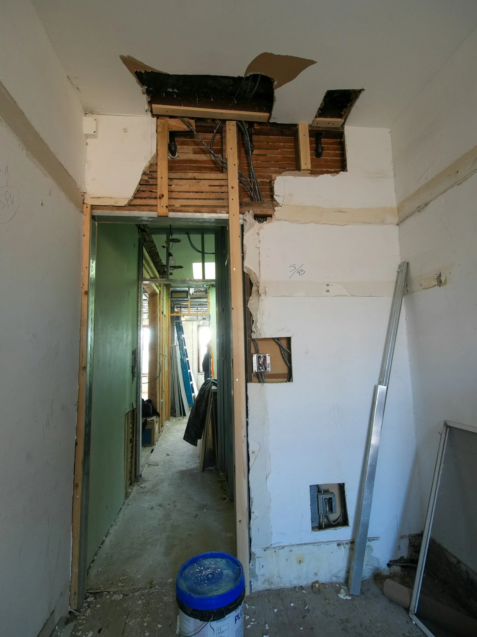 Construction site with exposed wall studs, electrical wiring, and partially removed drywall.