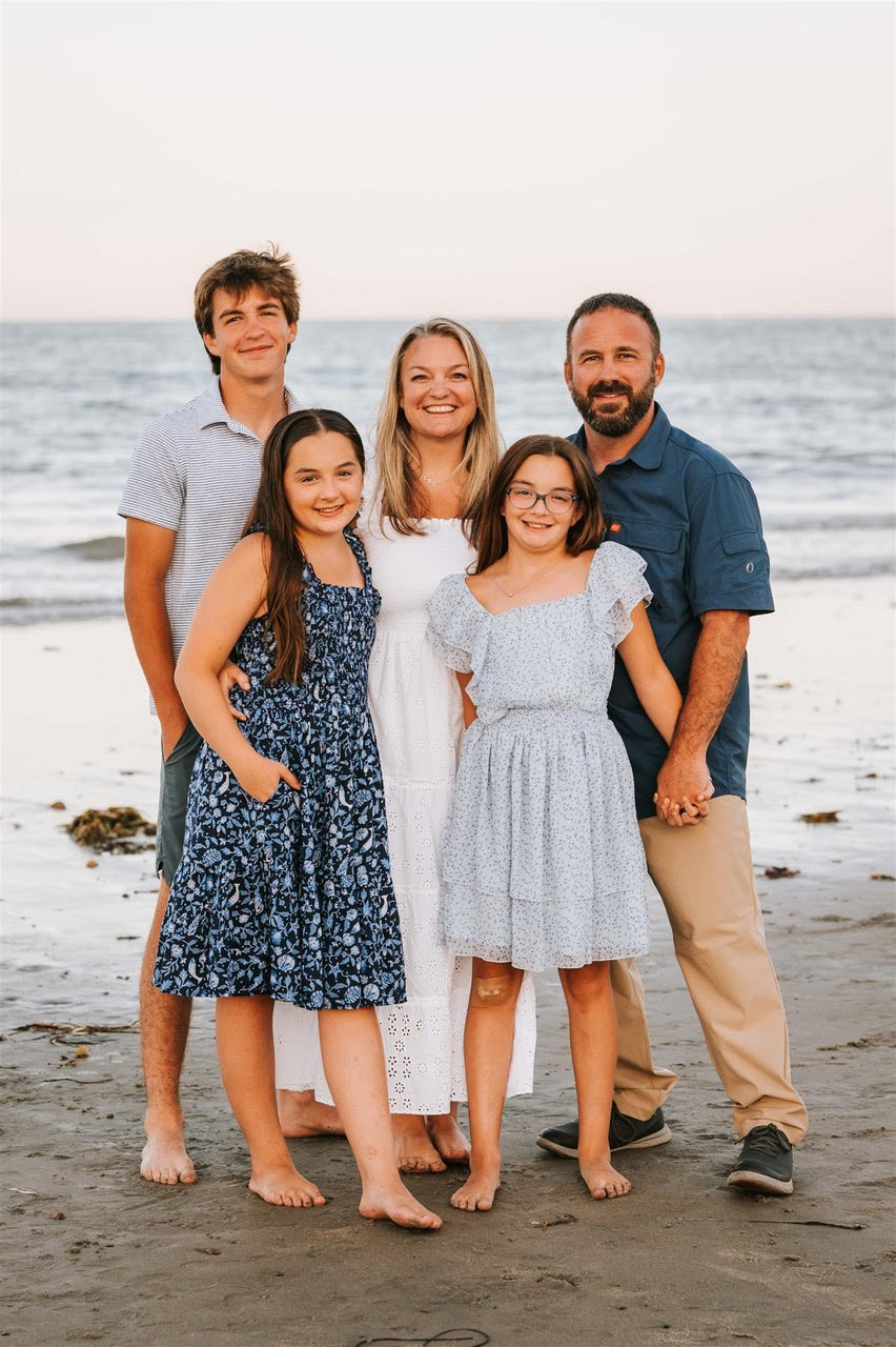 A family of six standing on a beach, holding hands and smiling at the camera, with the ocean in the background