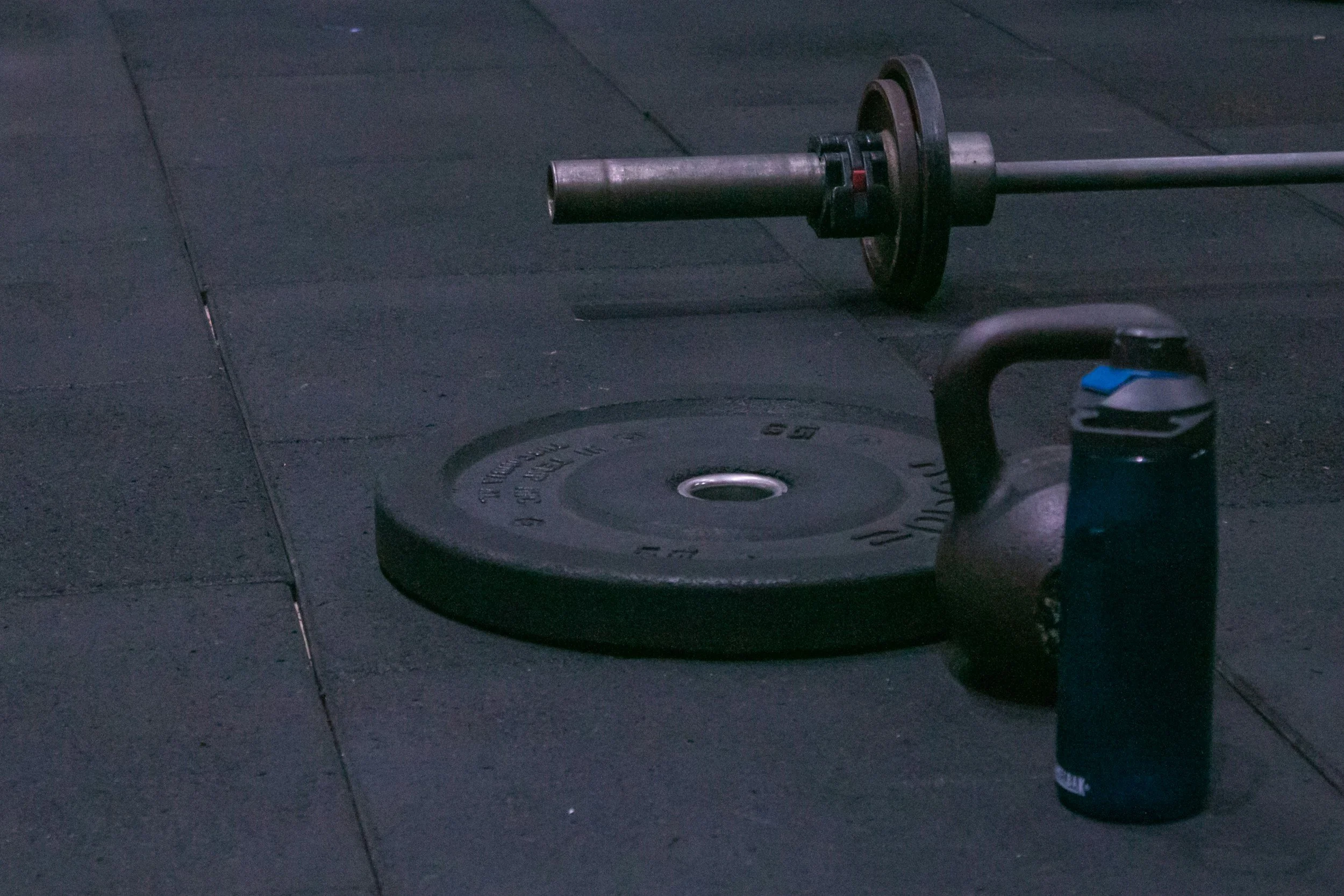 Hantelstange, Hantelscheibe, und Küchenpapier auf einem schwarzen Fitnessboden.