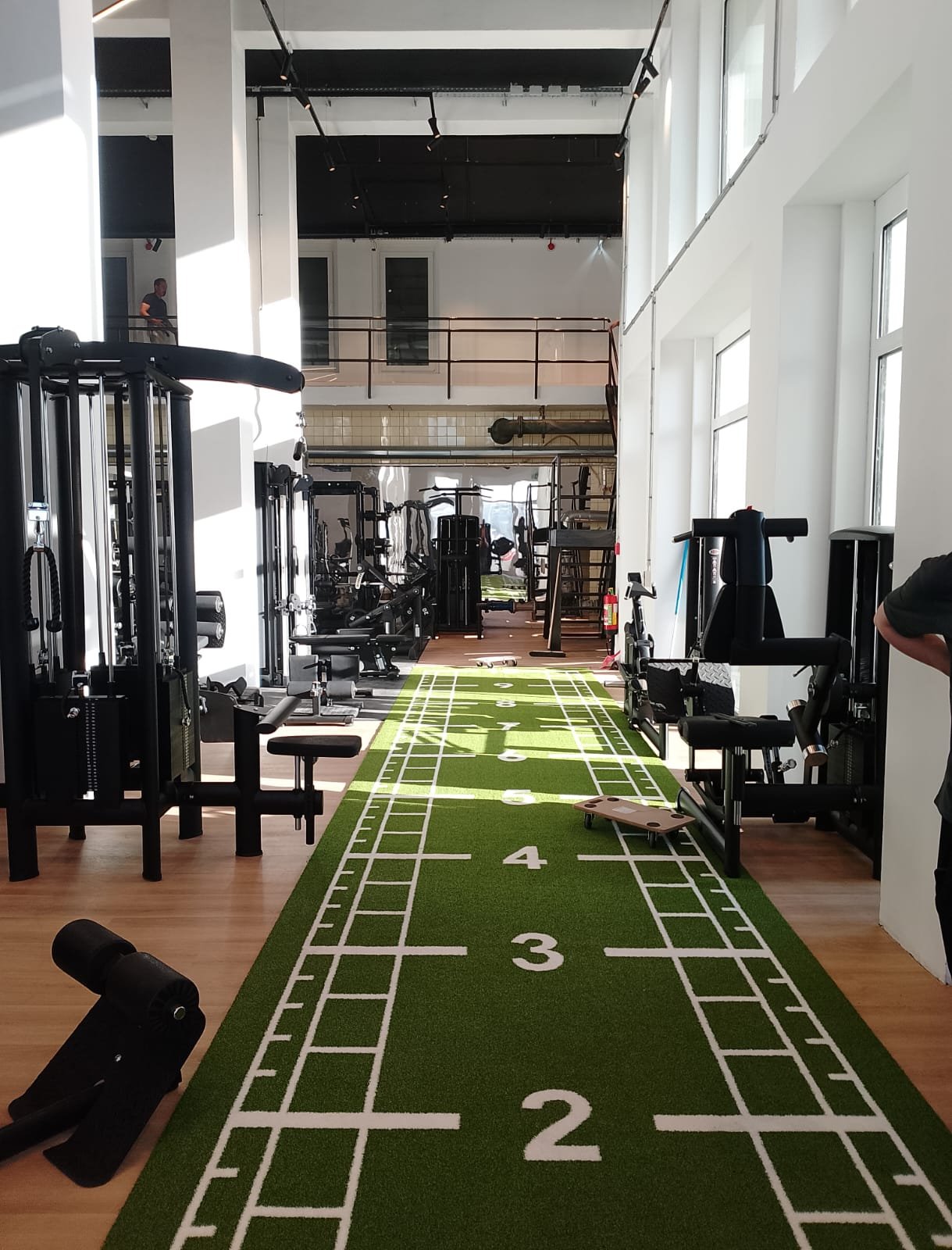 Indoor-Fitnessstudio mit Laufspur, Fitnessgeräte und Trainingsflächen, natürlichem Licht durch große Fenster.