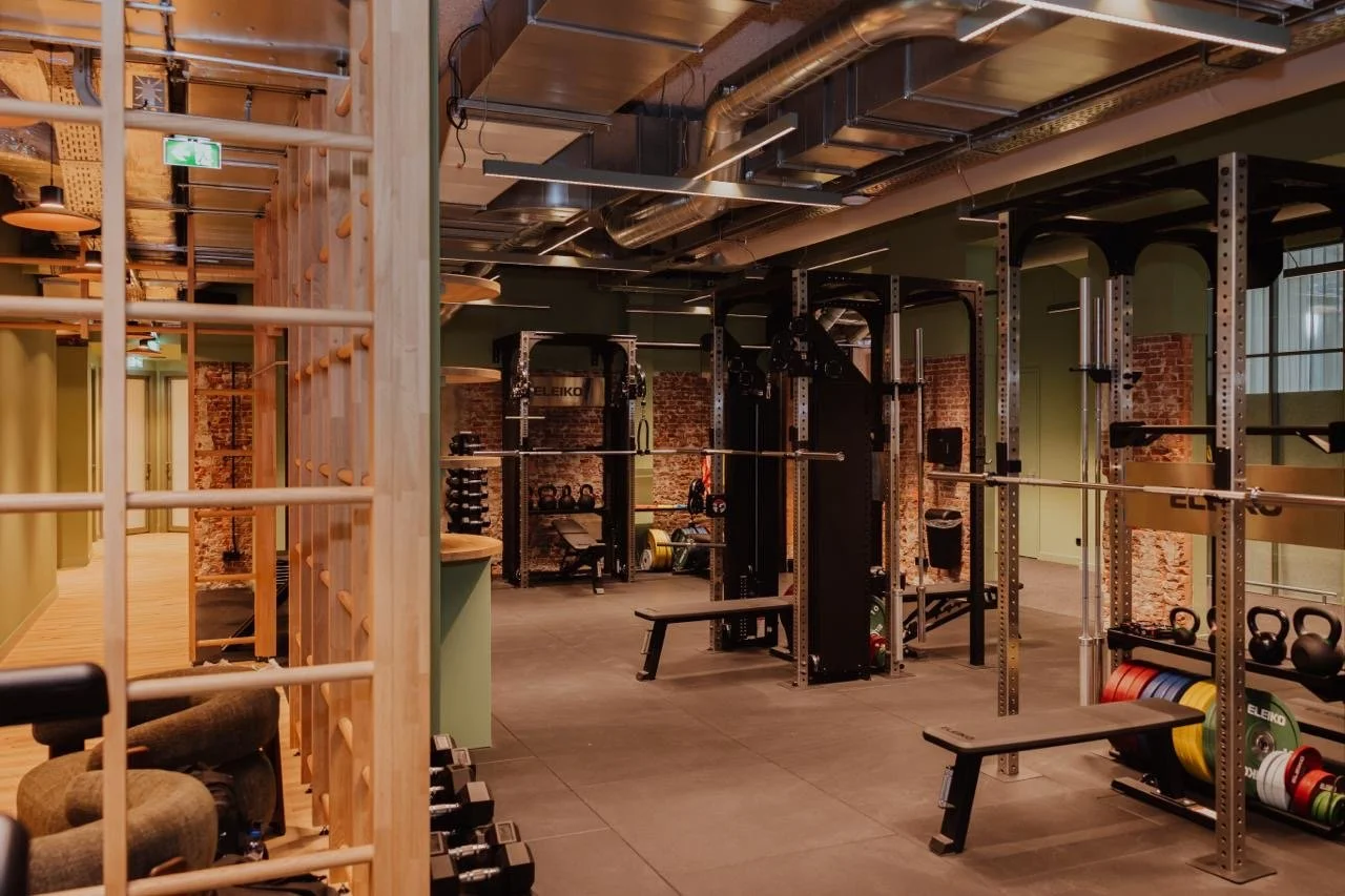 Ein Fitnessstudio mit Krafttrainingsgeräten, Hanteln und Langhanteln in einem Raum mit grünen Wänden, Backsteinwänden und industrialisiertem Deckenstil.