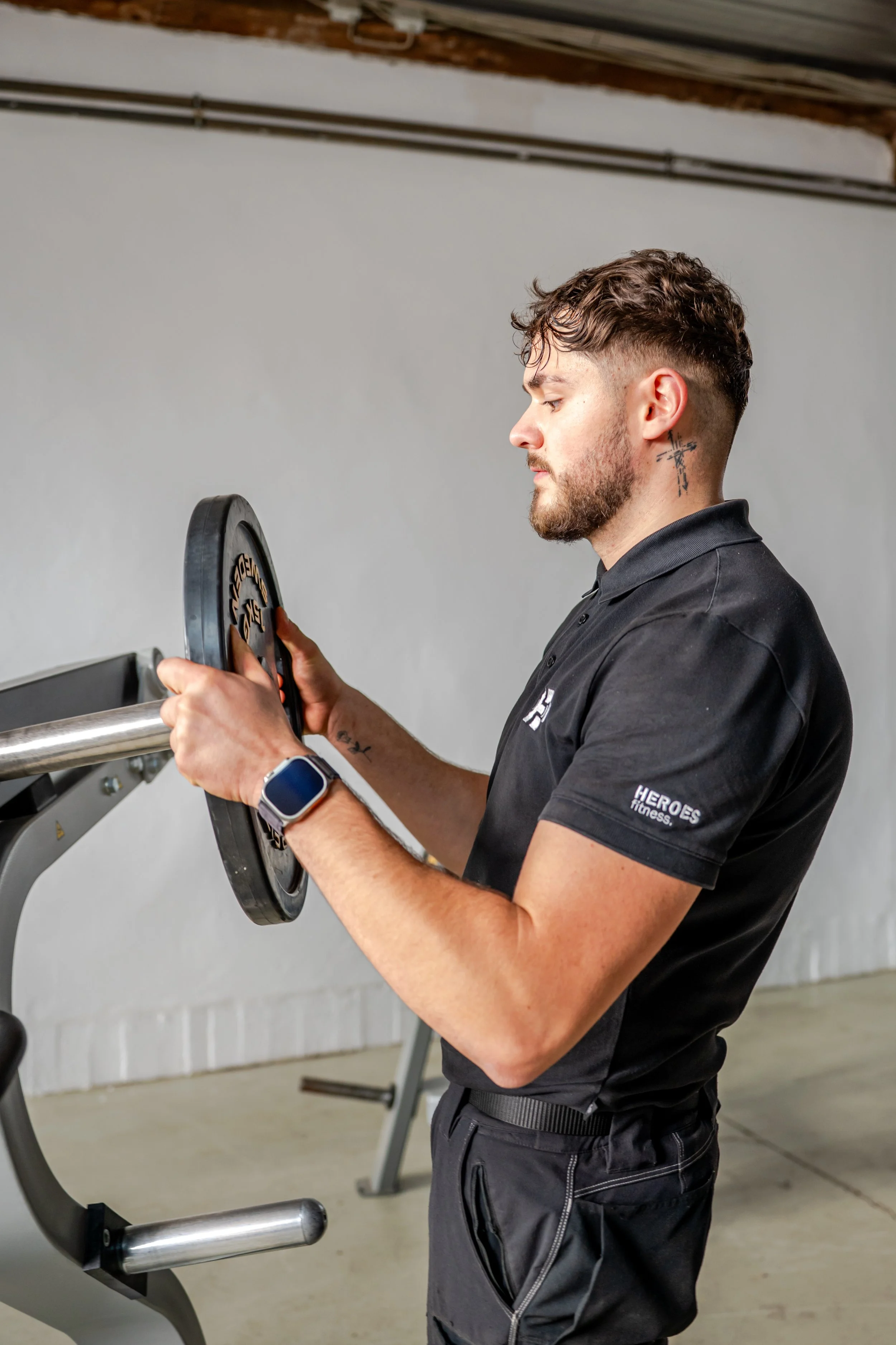 Ein männlicher Techniker mit Tattoo hebt eine Hantelscheibe bei einer Service-Leistung für ein Fitnessstudio.