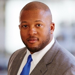 Portrait of a man in a suit with a blue tie, looking at the camera with a neutral expression.