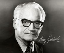 Black and white portrait of an older Barry Goldwater with white hair and glasses, wearing a suit and tie, with a serious expression.