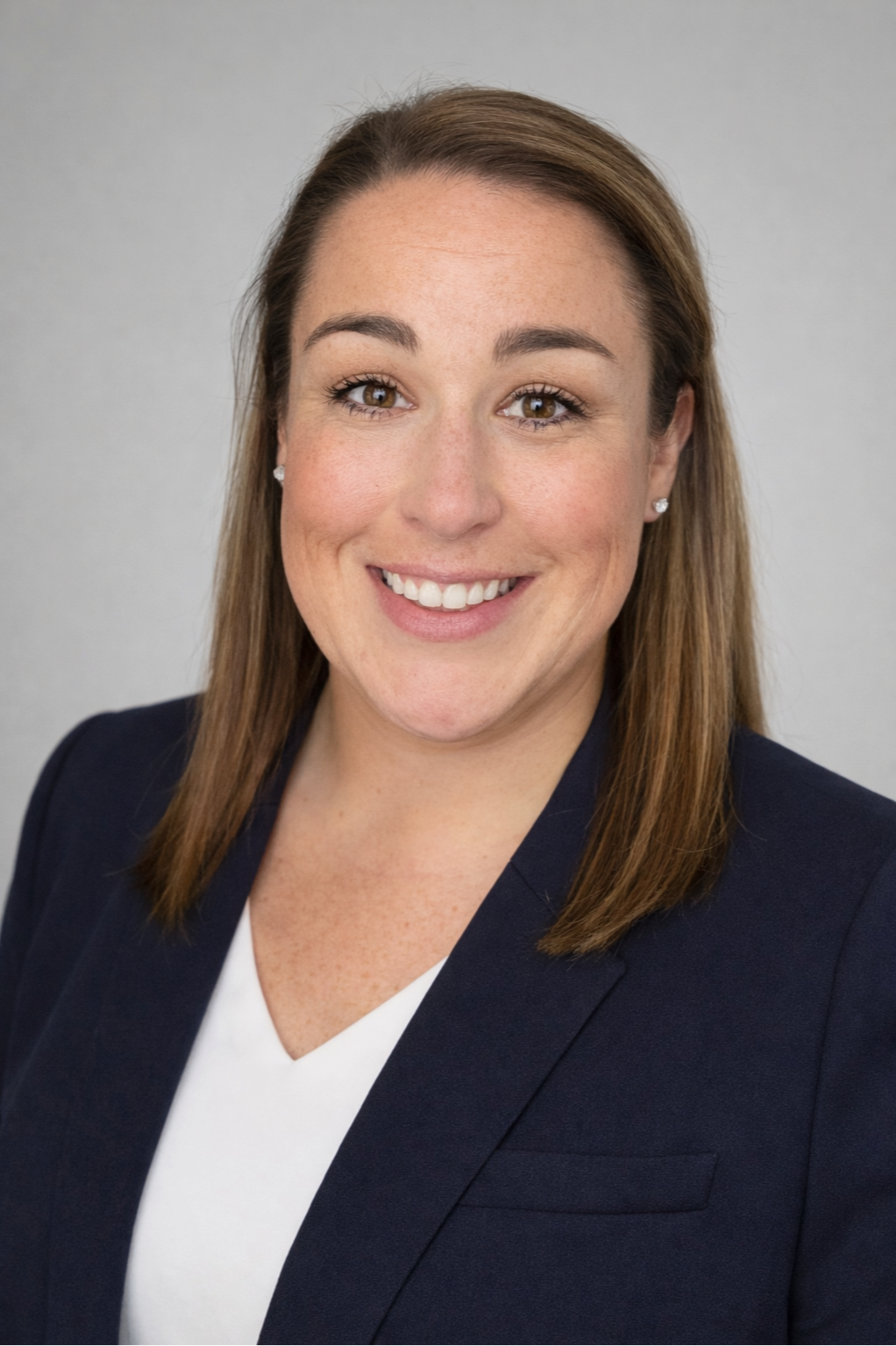 Professional woman with brown hair, wearing a dark blazer and white top, smiling against a neutral background.