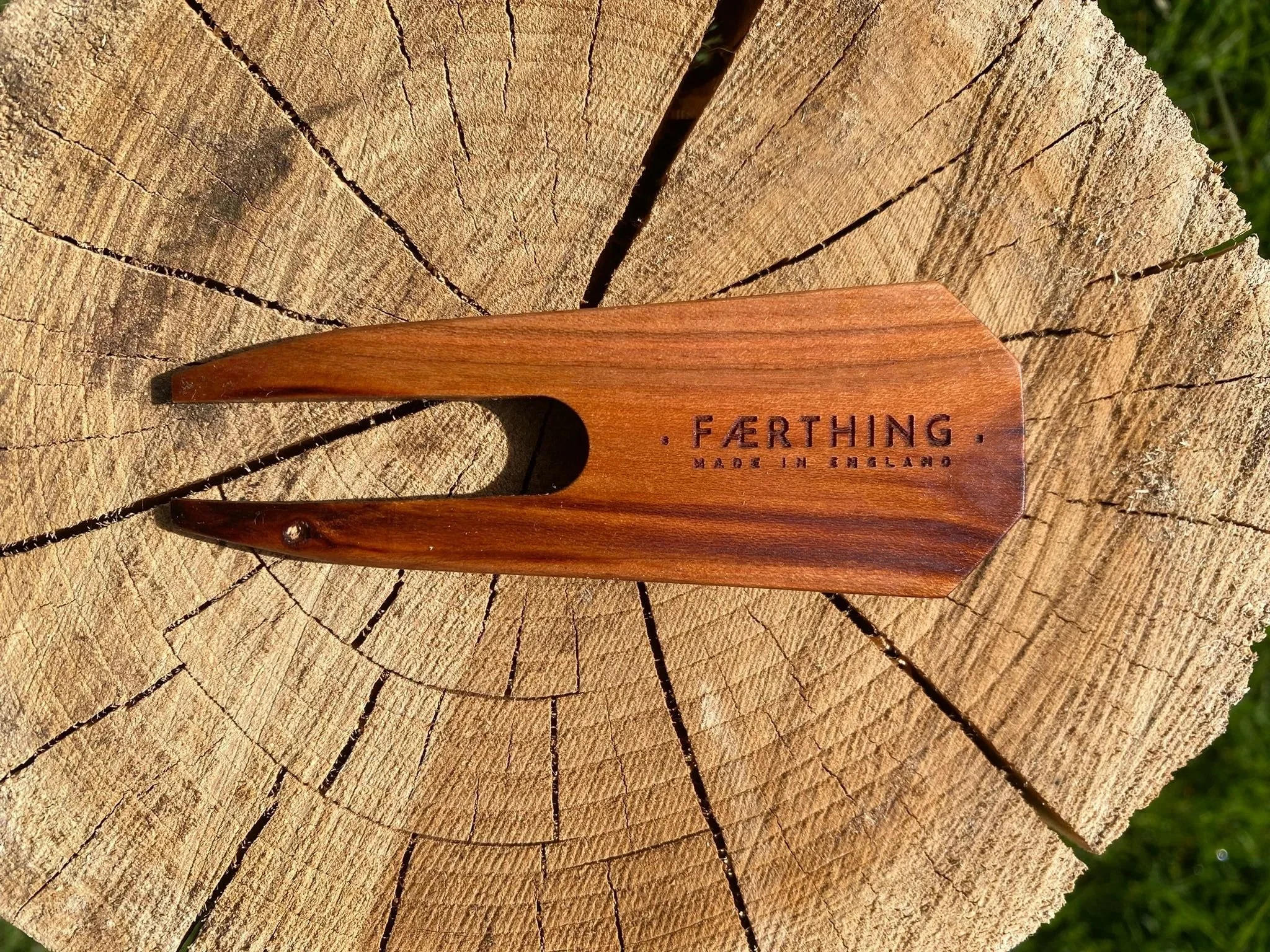 A wooden tool with a pointed end and a hole, engraved with the words 'FARTHING MADE IN ENGLAND,' resting on a tree stump.