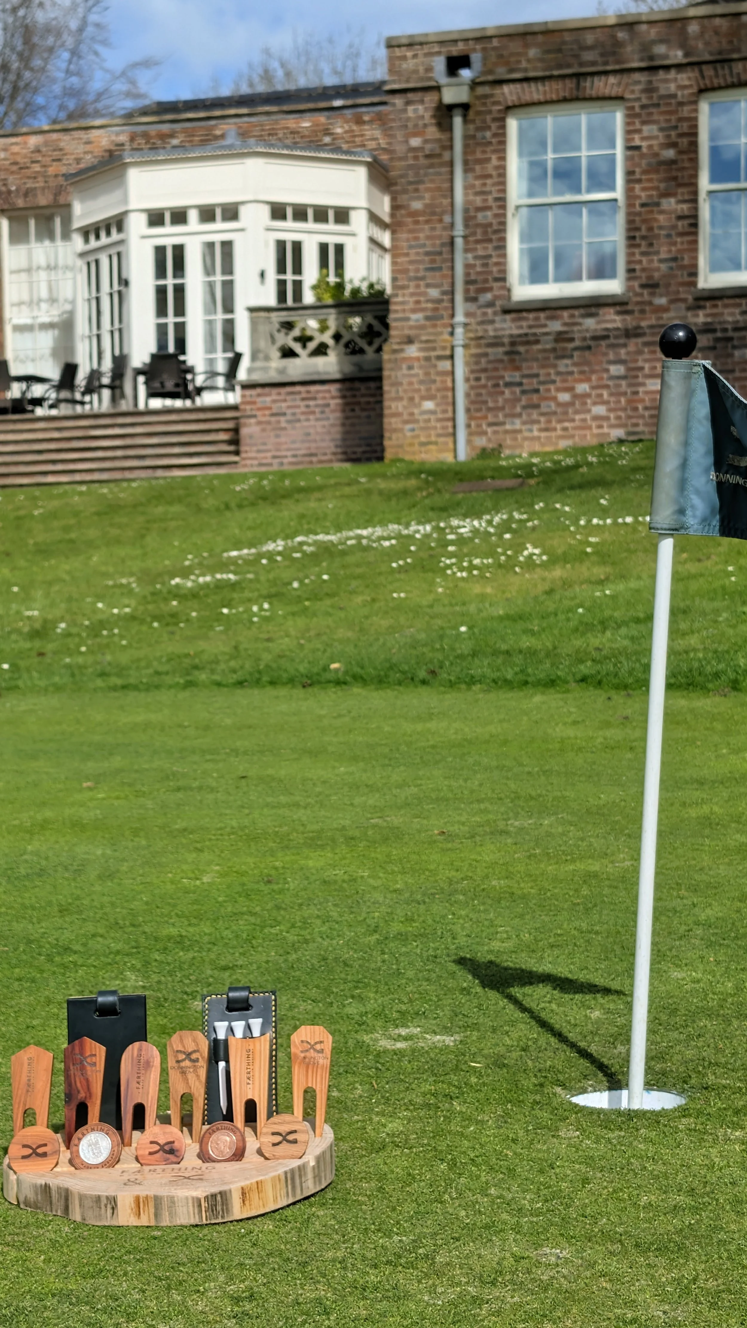 Golf putting practice area on a lawn with a flagstick and a wooden target with golf accessories.