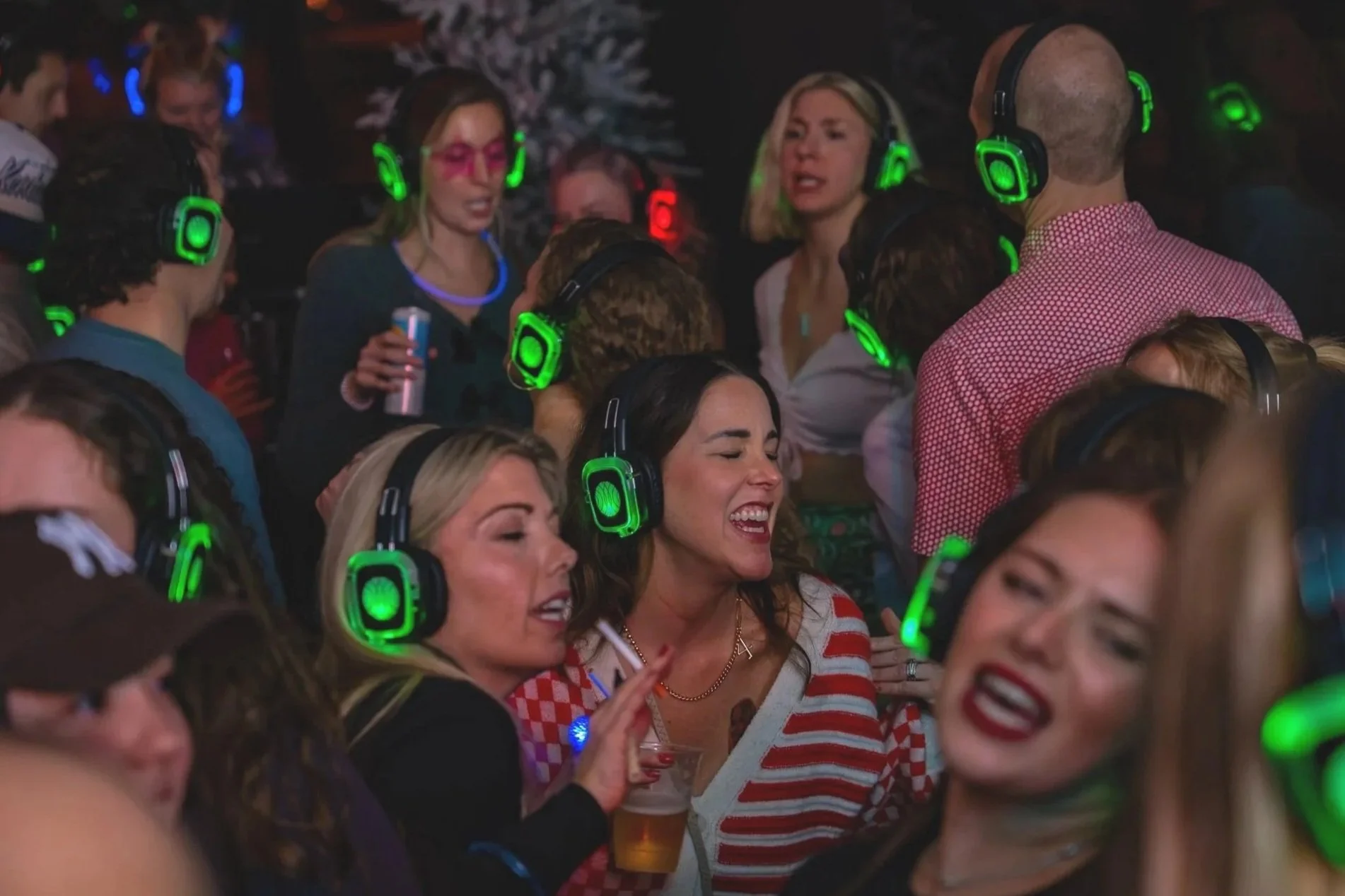 People dancing and singing at a party, wearing green and black headphones.