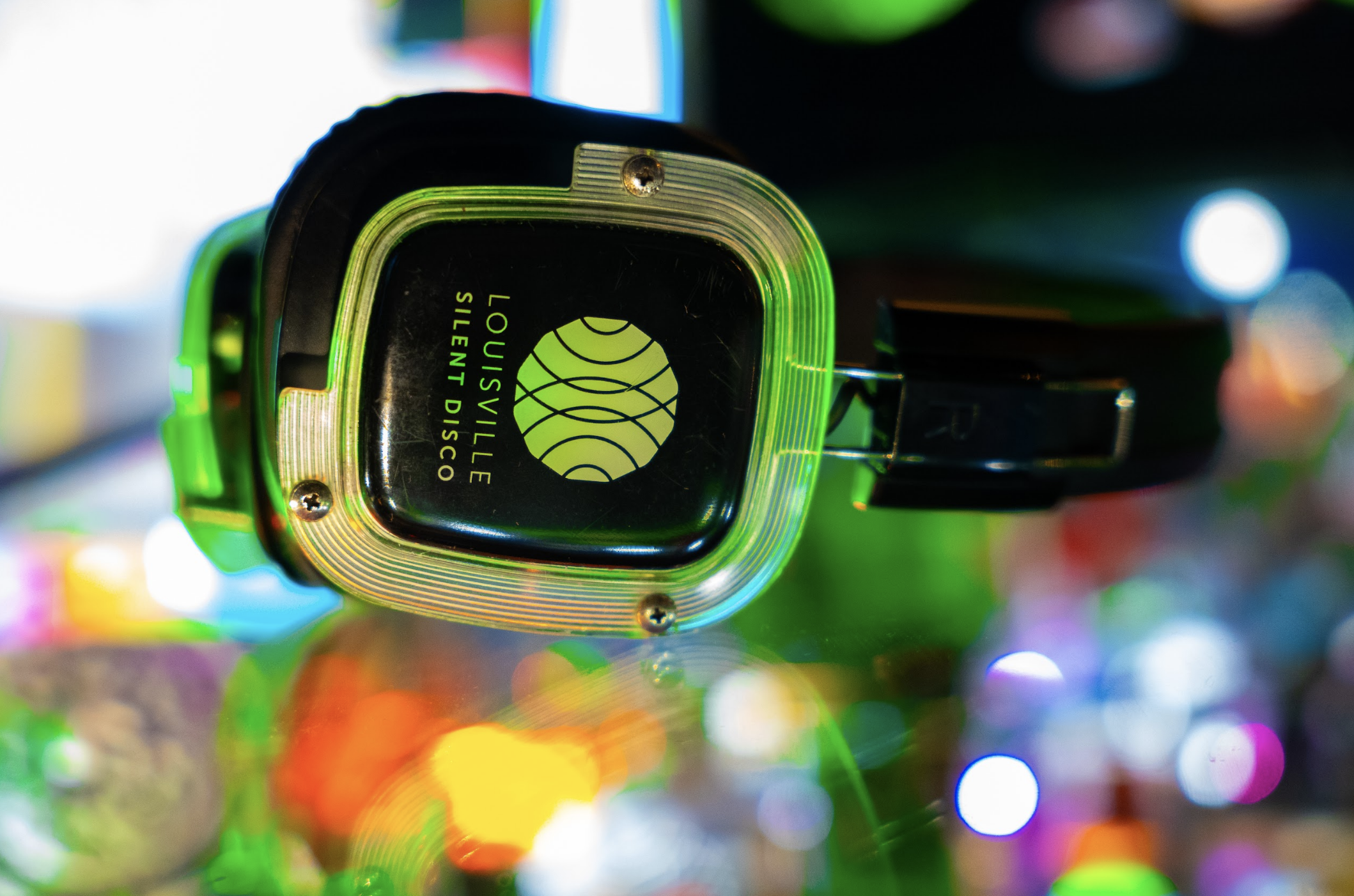 Close-up of a square-shaped electronic device with a black screen displaying a logo and text, with colorful blurred lights in the background.