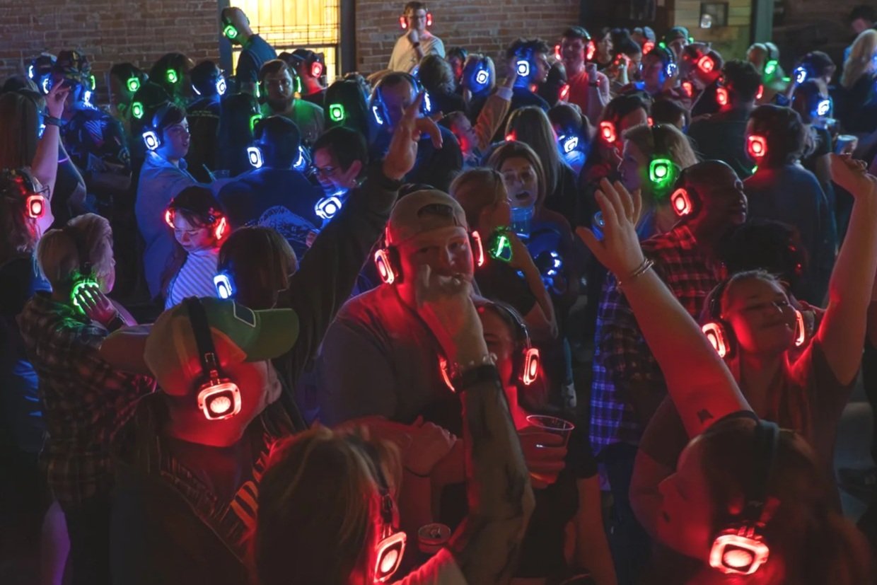 People dancing and enjoying music with colorful LED headphones at a party or music event indoors.