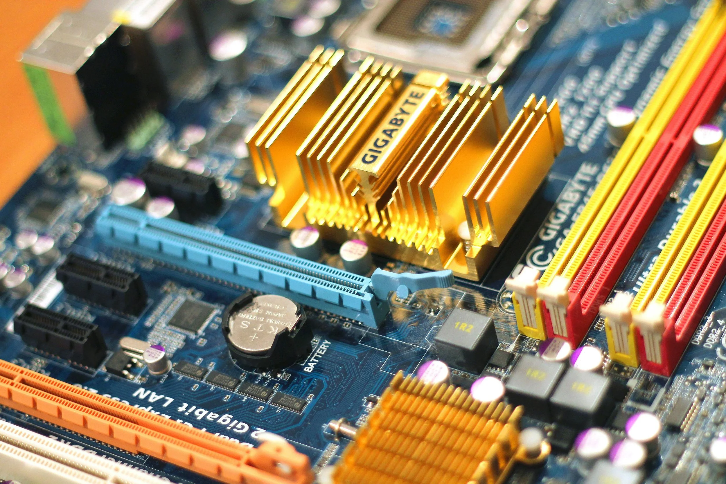 Close-up of a computer motherboard with a gold heat sink labeled GIGABYTE, colorful RAM slots, and various electronic components.