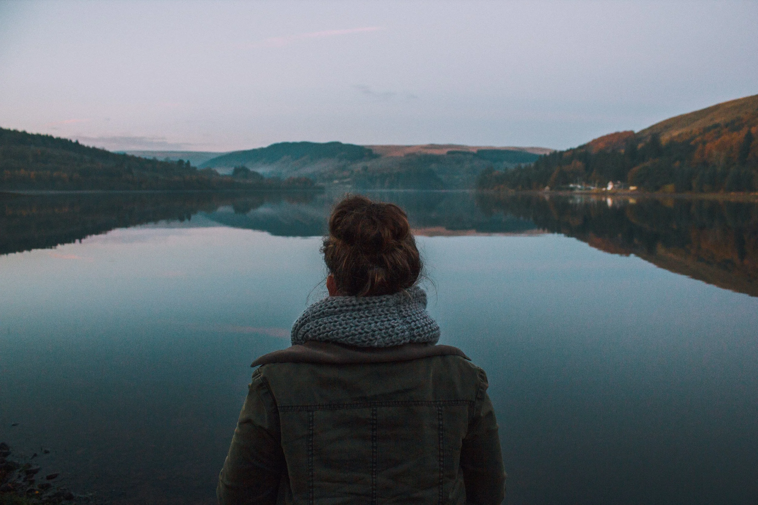 Woman with her back turned looking at a peaceful lake with moutains