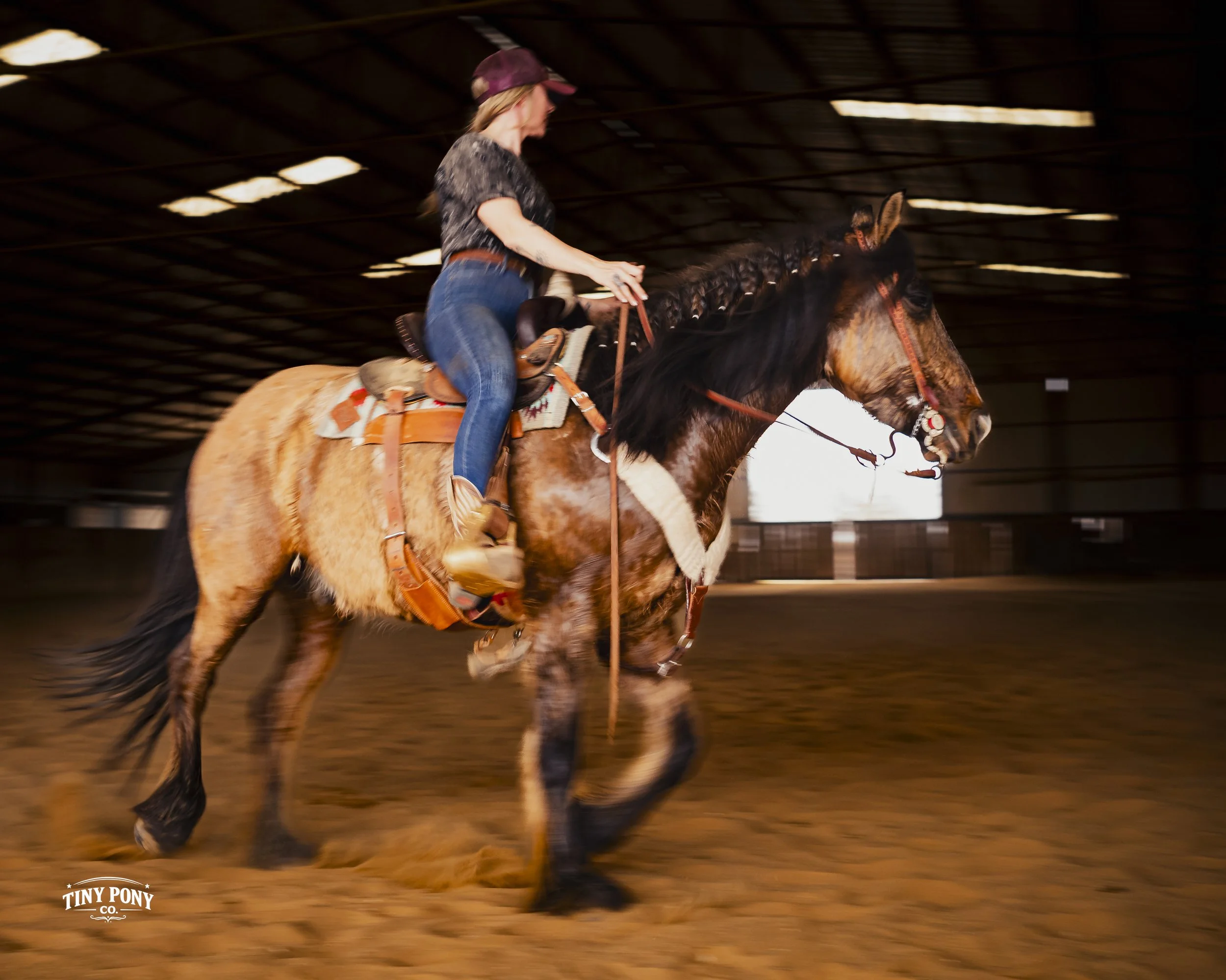 A woman riding a galloping horse inside an indoor riding arena.