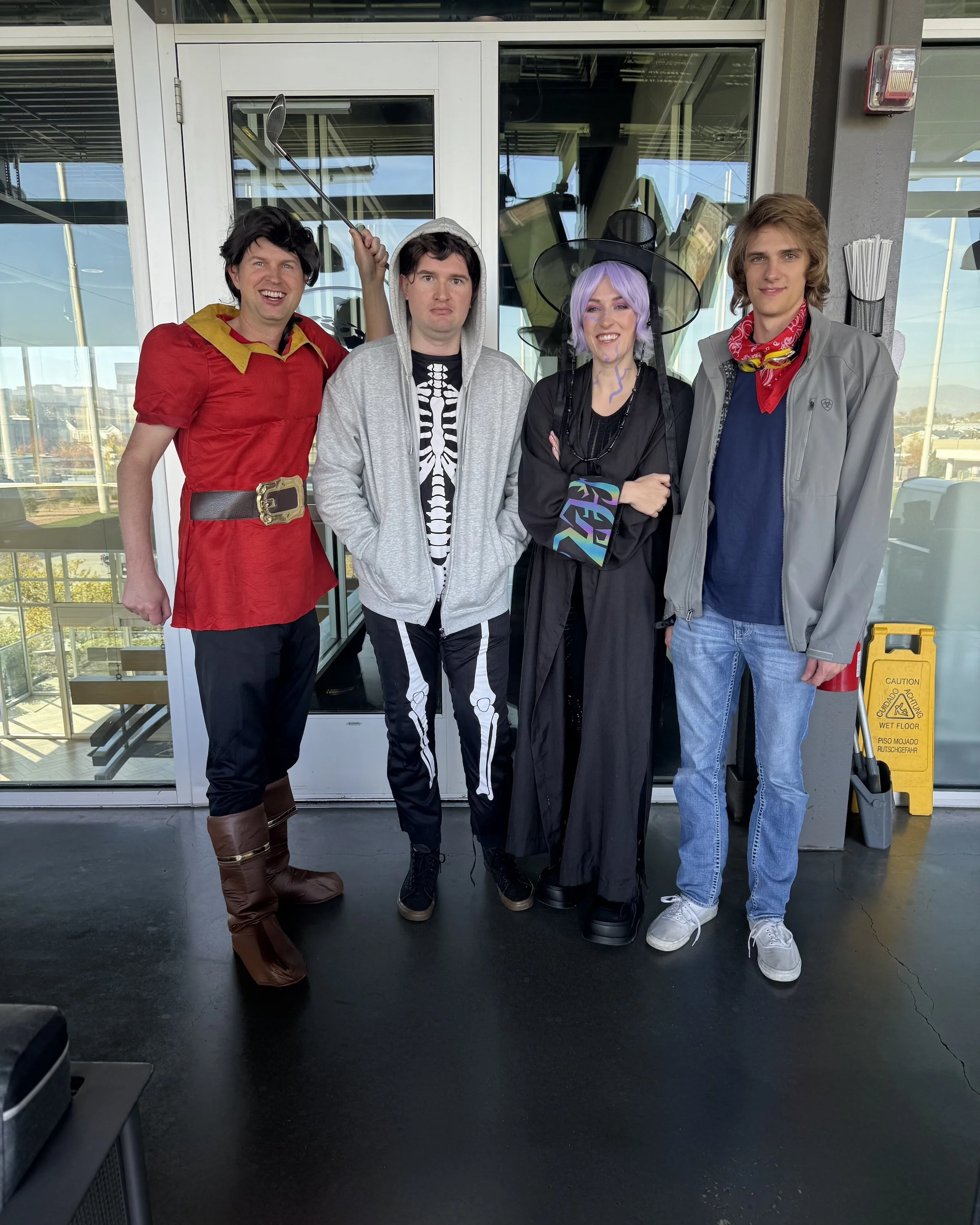 Four people dressed in costumes standing together outside a building with glass doors and windows.