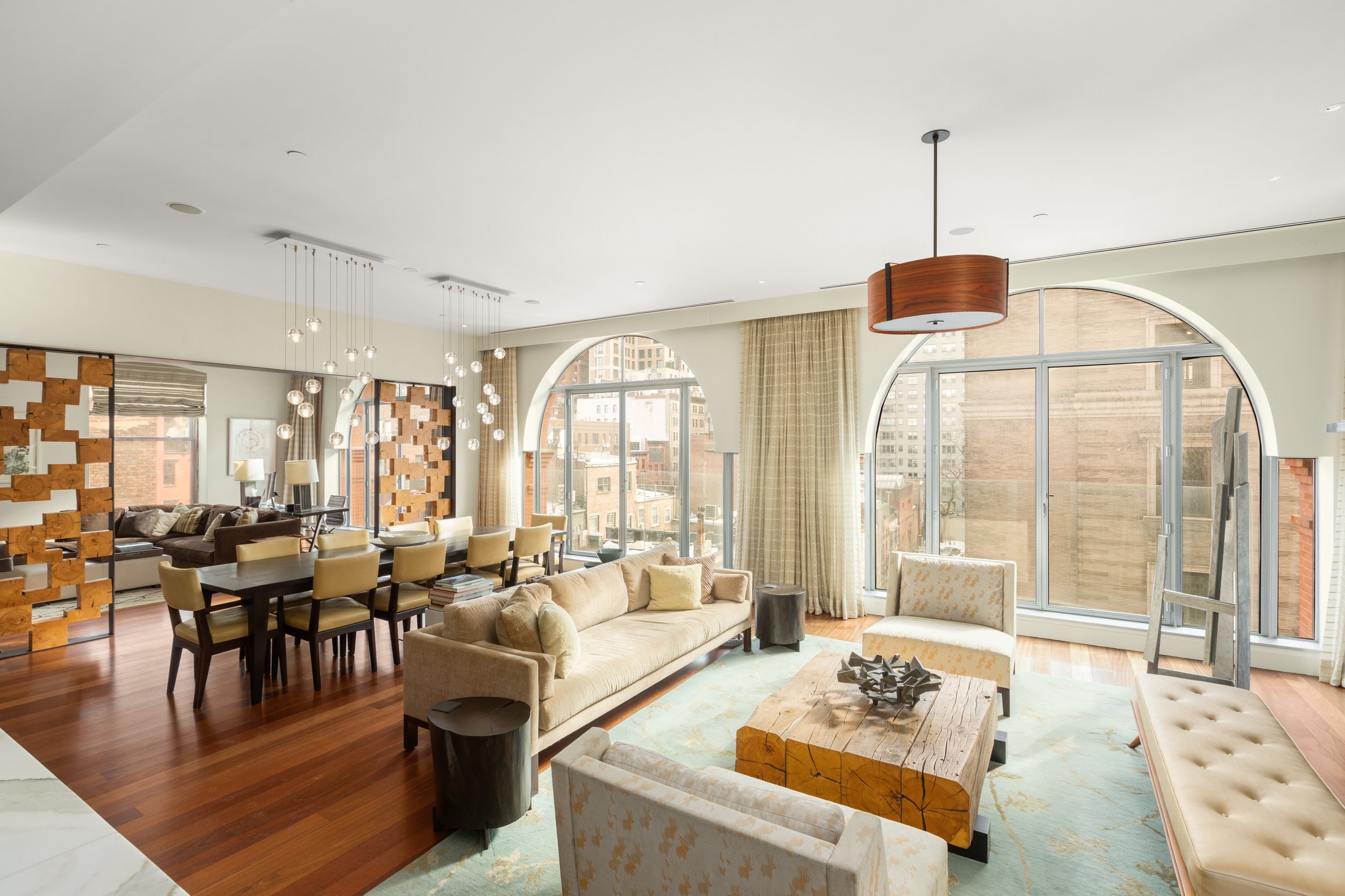 Bright and spacious living room with large arched windows, beige sofas, armchairs, a wooden coffee table, and modern lighting fixtures.