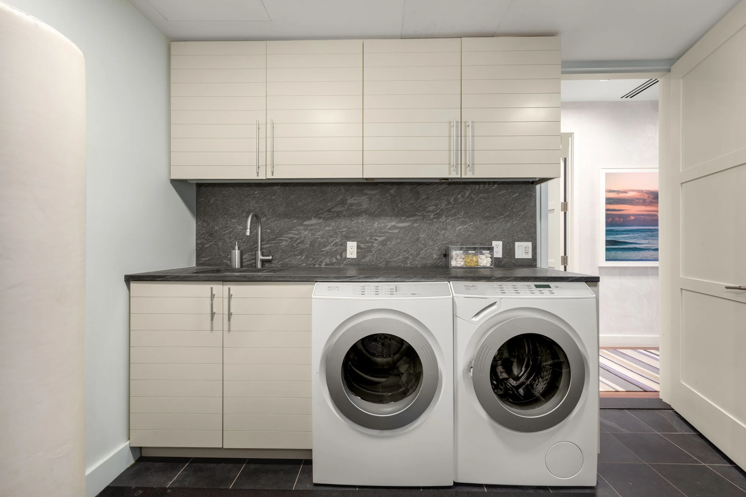 Laundry room with white washer and dryer, grey cabinet, granite countertop, and a sink.