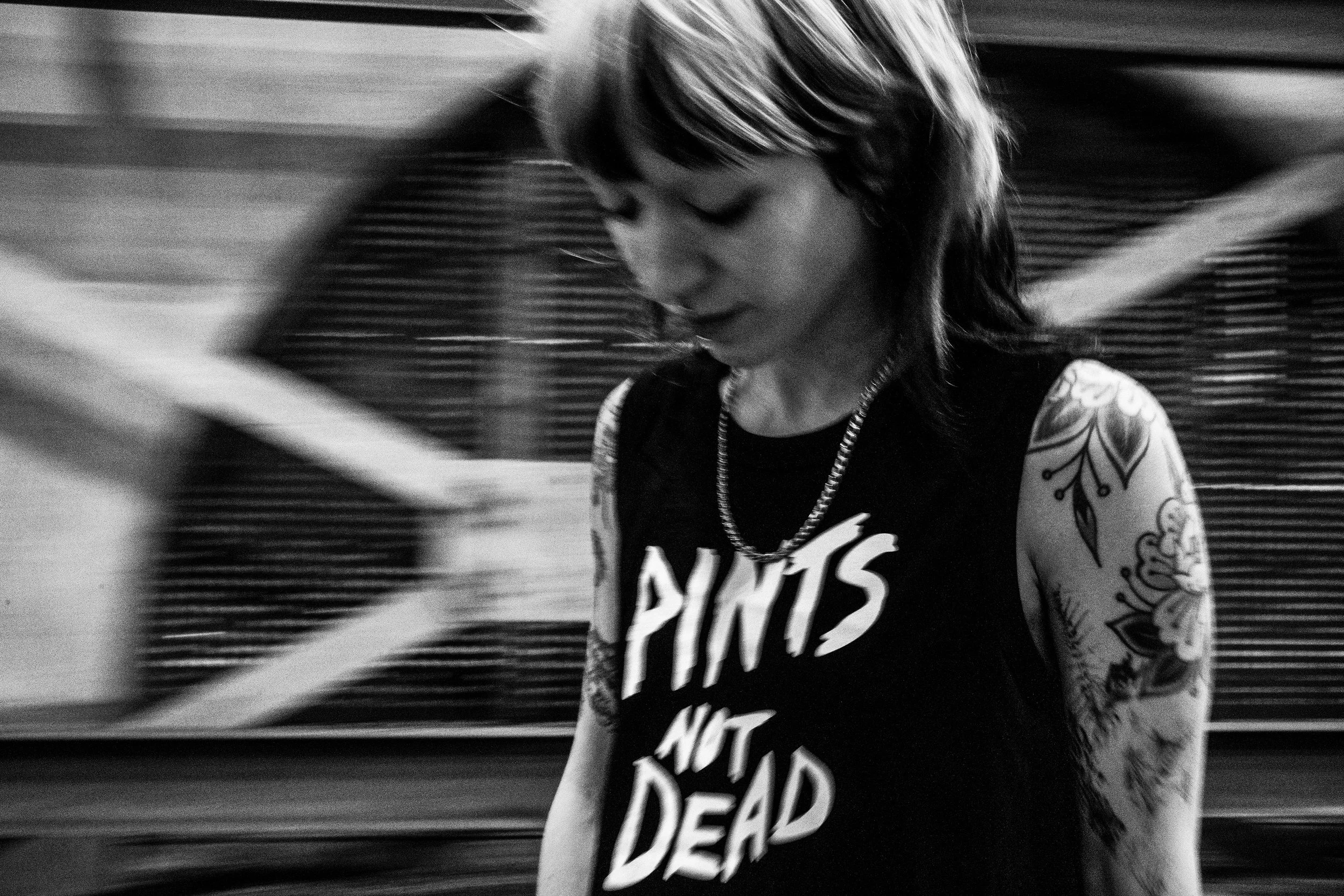 Skateboarder Alice wearing Courier Brewing Co. "Pint Not Dead" tank top in a car park in Manchester UK