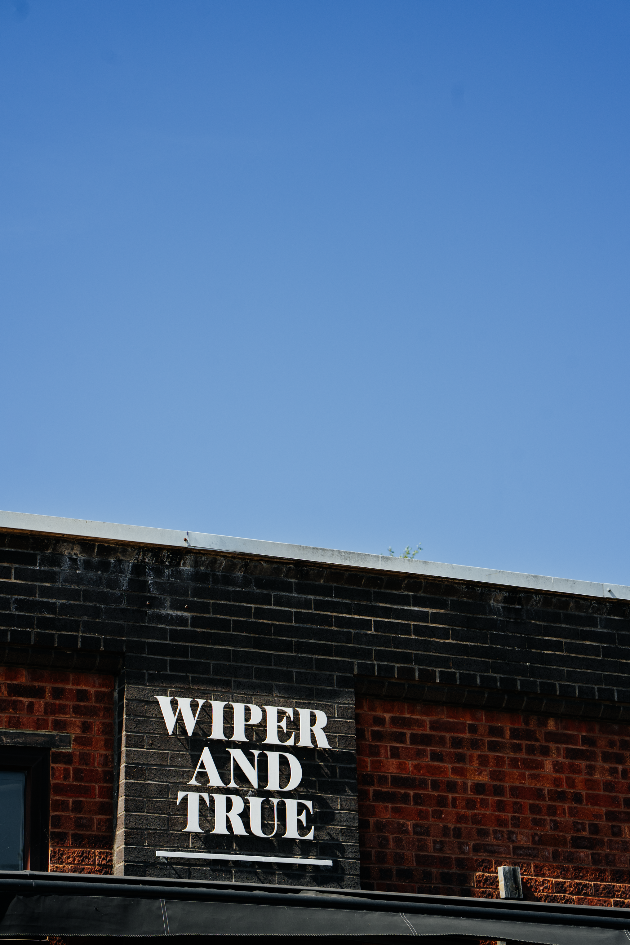 Close-up of a sign on a brick building that reads 'WIPER AND TRUE' under a blue sky.