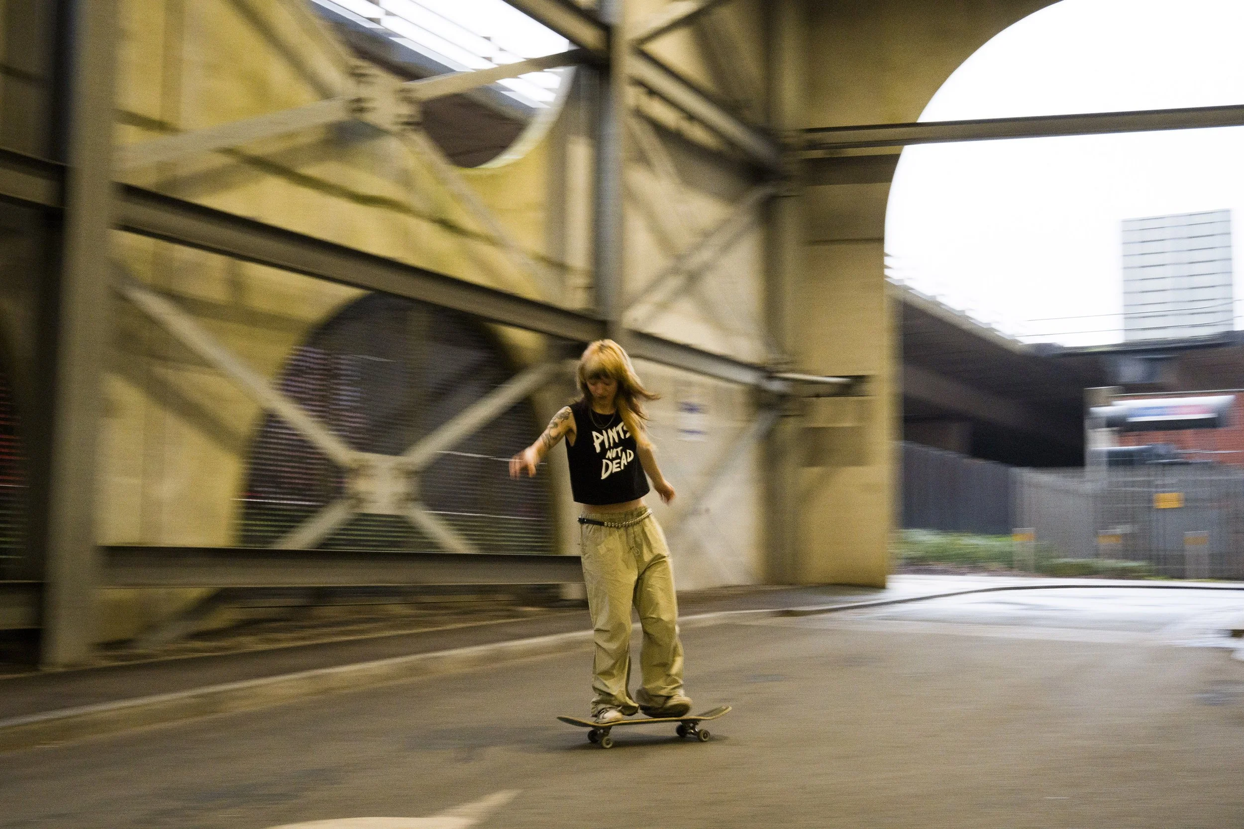 Alice skateboarding in Manchester wearing "Pints Not Dead" Courier Brewing t-shirt