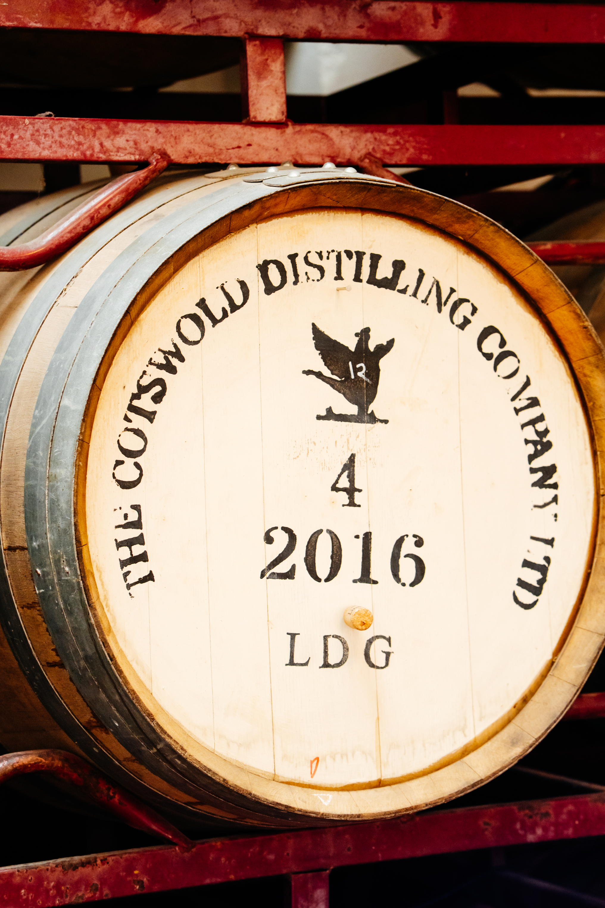 A vintage whiskey distilling company clock from 2016, featuring a bird logo, mounted inside a red metal frame in Wiper & True Barrel Store