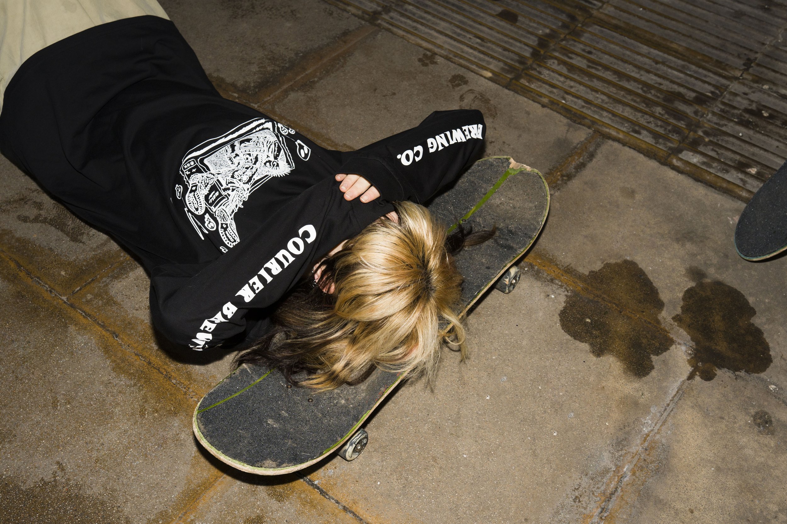 Alice laying on a skateboard wearing long sleeve Courier Brewing Co t-shirt for a merch shoot in Manchester, UK