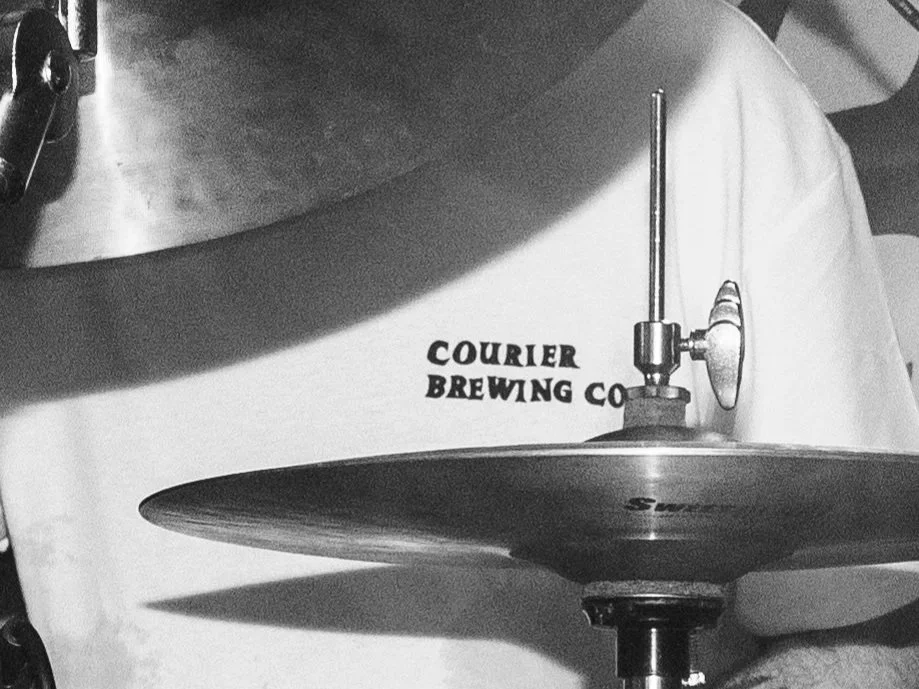 Close up of Courier Brewing Co logo on a t-shirt shot through a drum kit at a Bruise Control gig in Manchester, UK