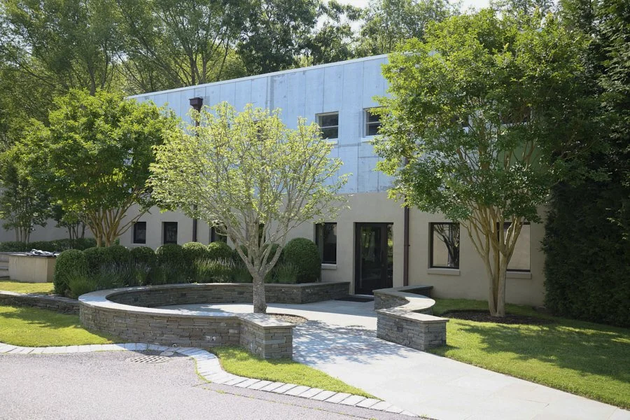 Modern building with trees, shrubs, and a curved stone bench in the front yard.