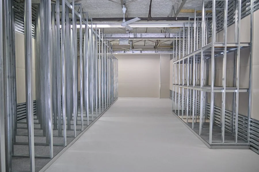 Empty metal framing walls in a construction site, with construction materials and equipment on the ceiling.