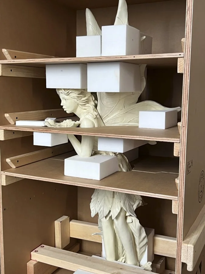 A large fairy sculpture inside a storage box surrounded by white foam blocks for protection.