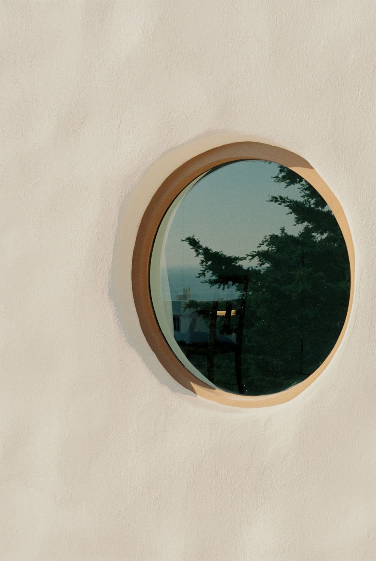 a reflection of the ocean and a house and trees through a circular exterior window-bordered
