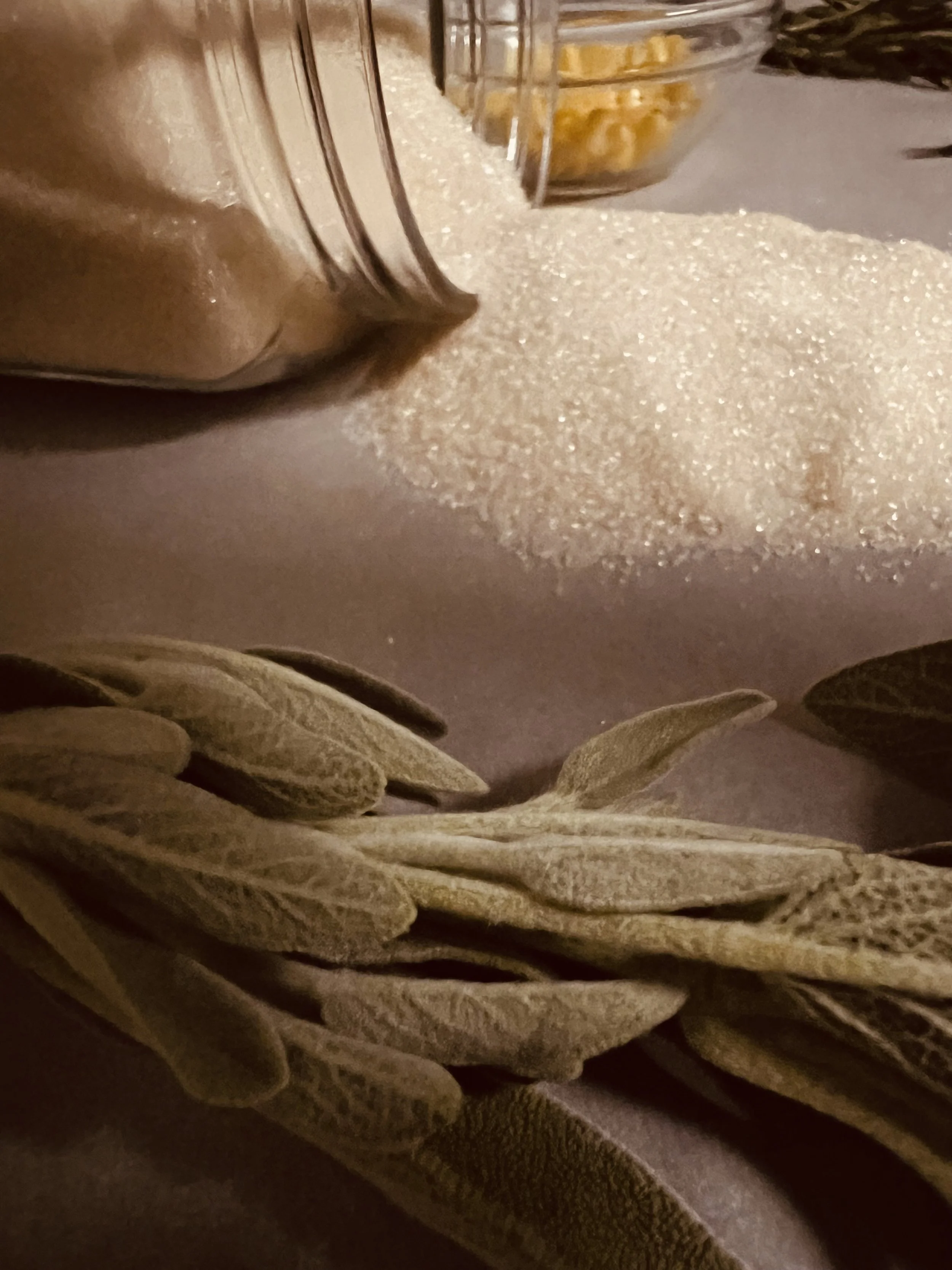 Dried sage leaves, a glass bowl of sugar, and salt shaker on a table.