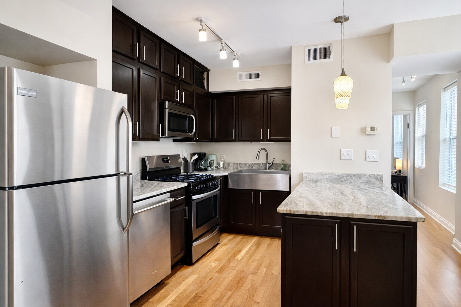 Modern kitchen with dark wood cabinets, stainless steel appliances, and a marble countertop island.