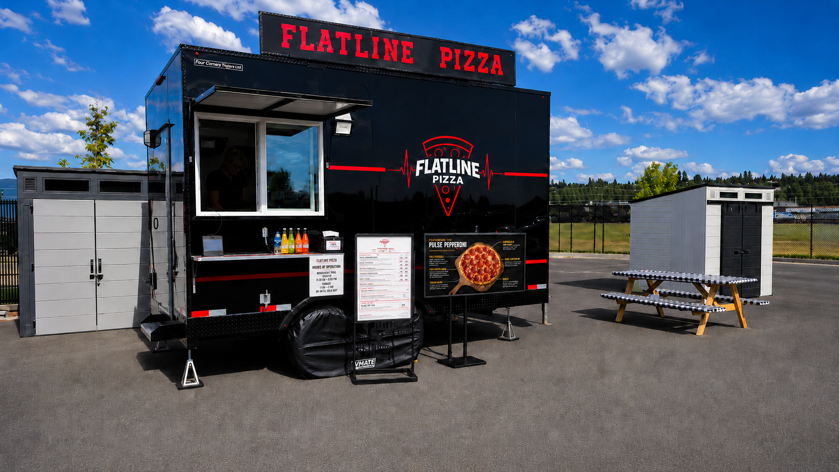 Black pizza food truck with red and white graphics, including a pizza slice and a heartbeat line, parked on a dirt surface surrounded by trees and a partly cloudy sky.