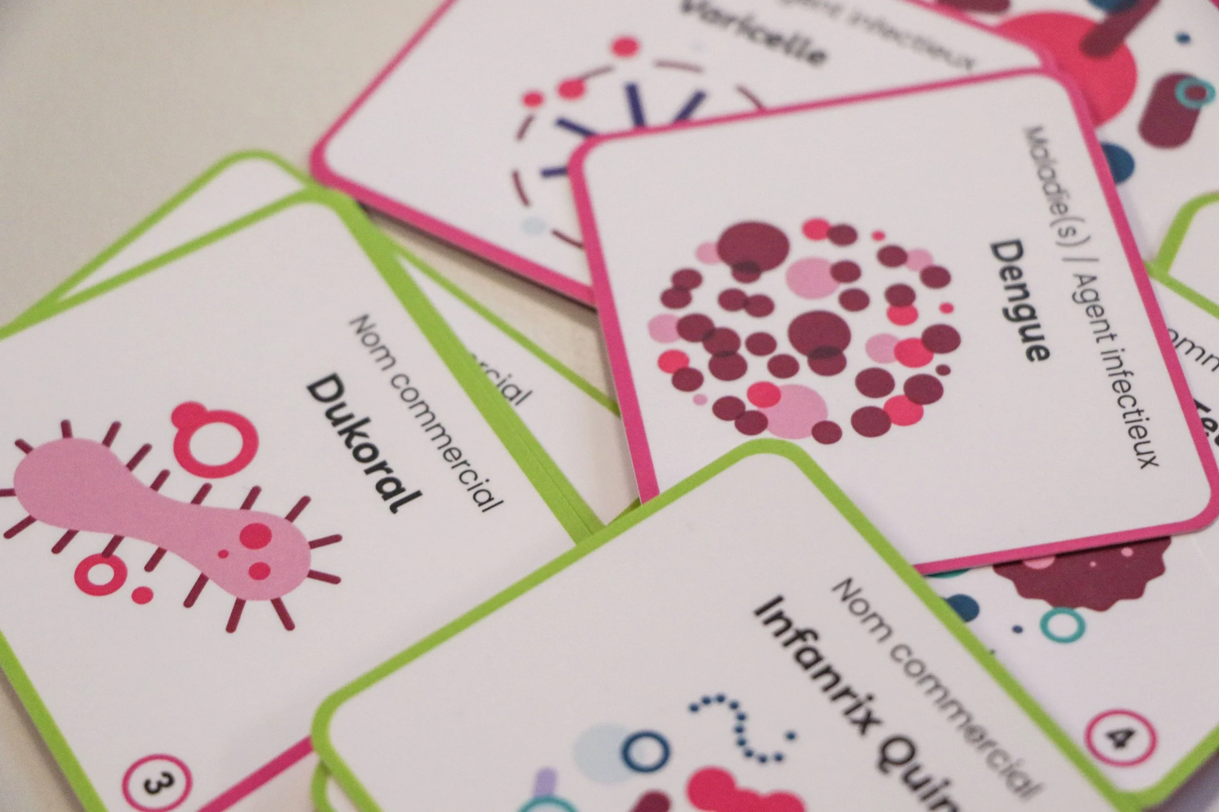 Vue du dessus montrant l'ensemble des cartes du jeu sur la vaccination étalées à côté de leur étui sur une table en bois clair.