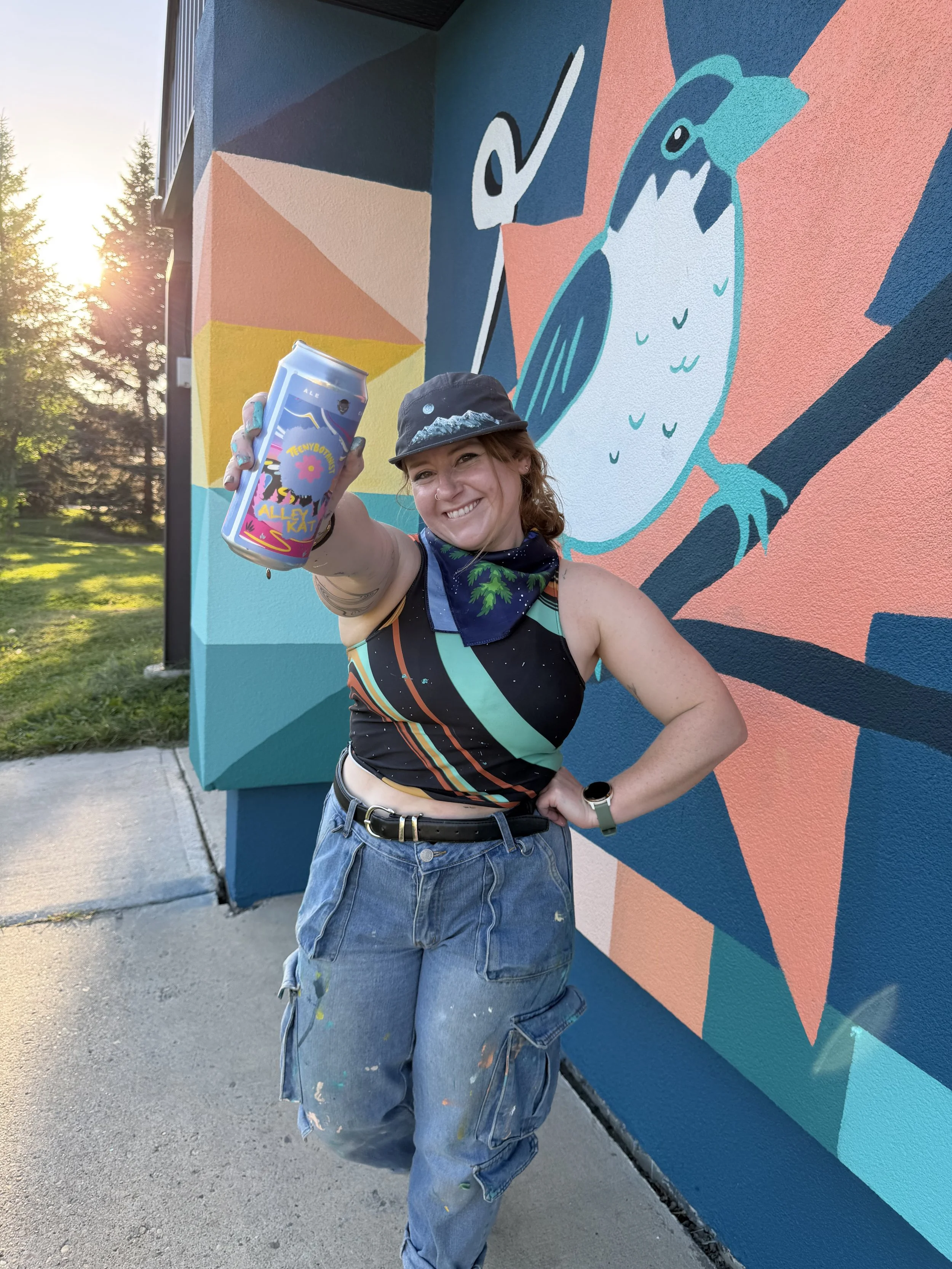 Teenybotanist holding an Alley Kat can in front of a mural
