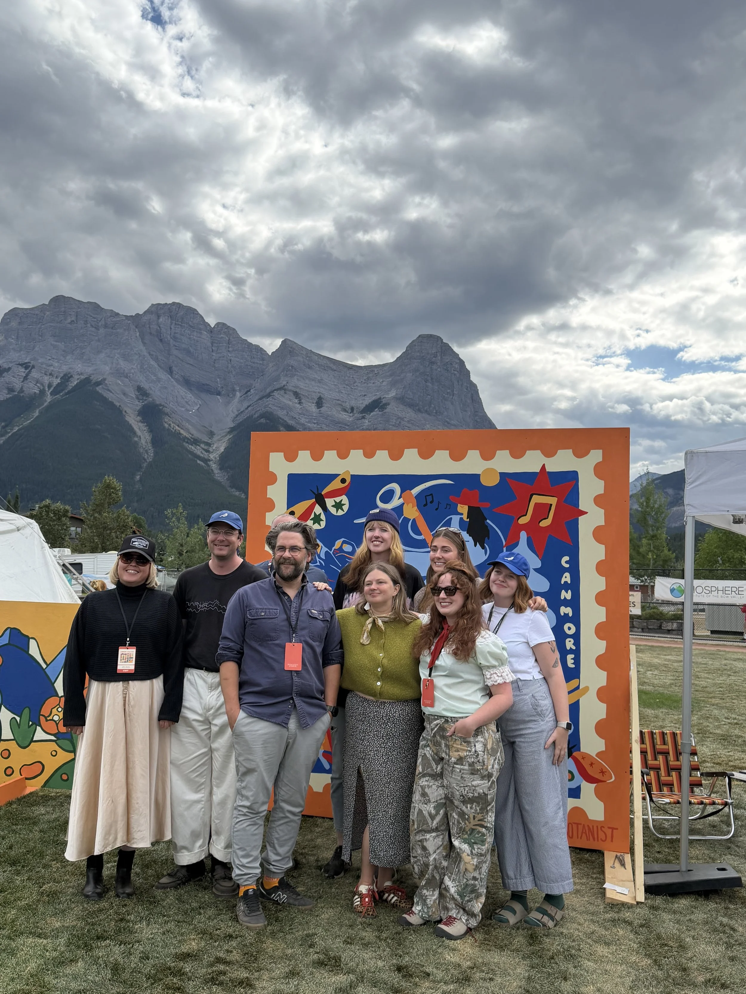 Group photo in front of the Out of Office mural at Canmore Folk Festival