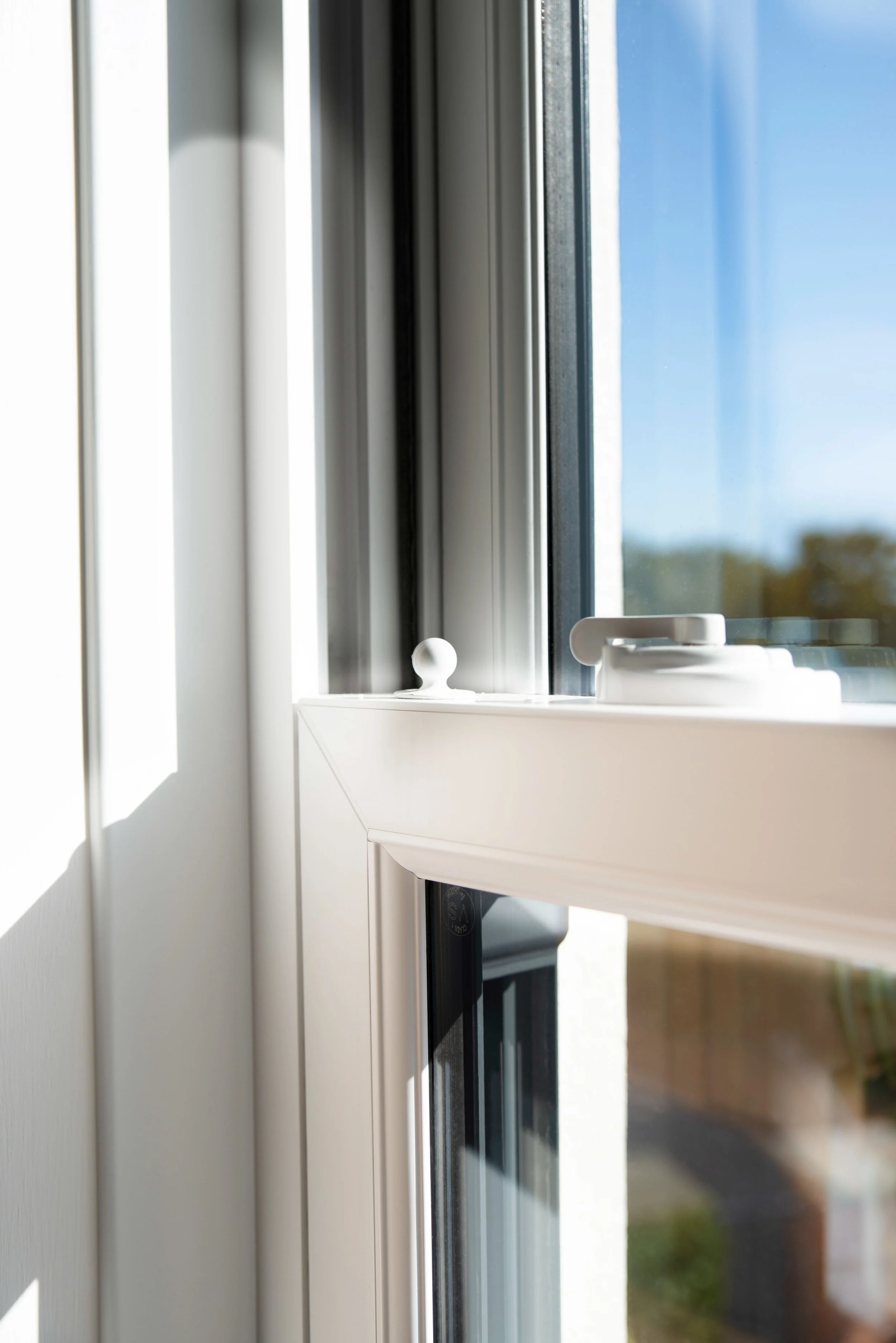 Close-up of a white window latch on a glass window with sunlight casting shadows inside a room.