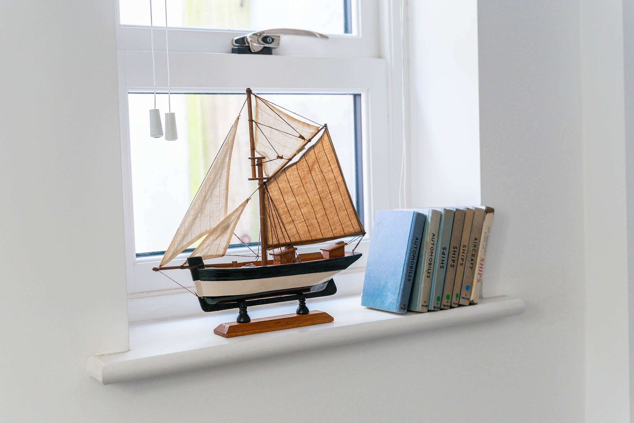 Holiday let in Brixham with a model sailboat decor with tan sails, positioned on a window sill next to a row of books and a small window in the background.