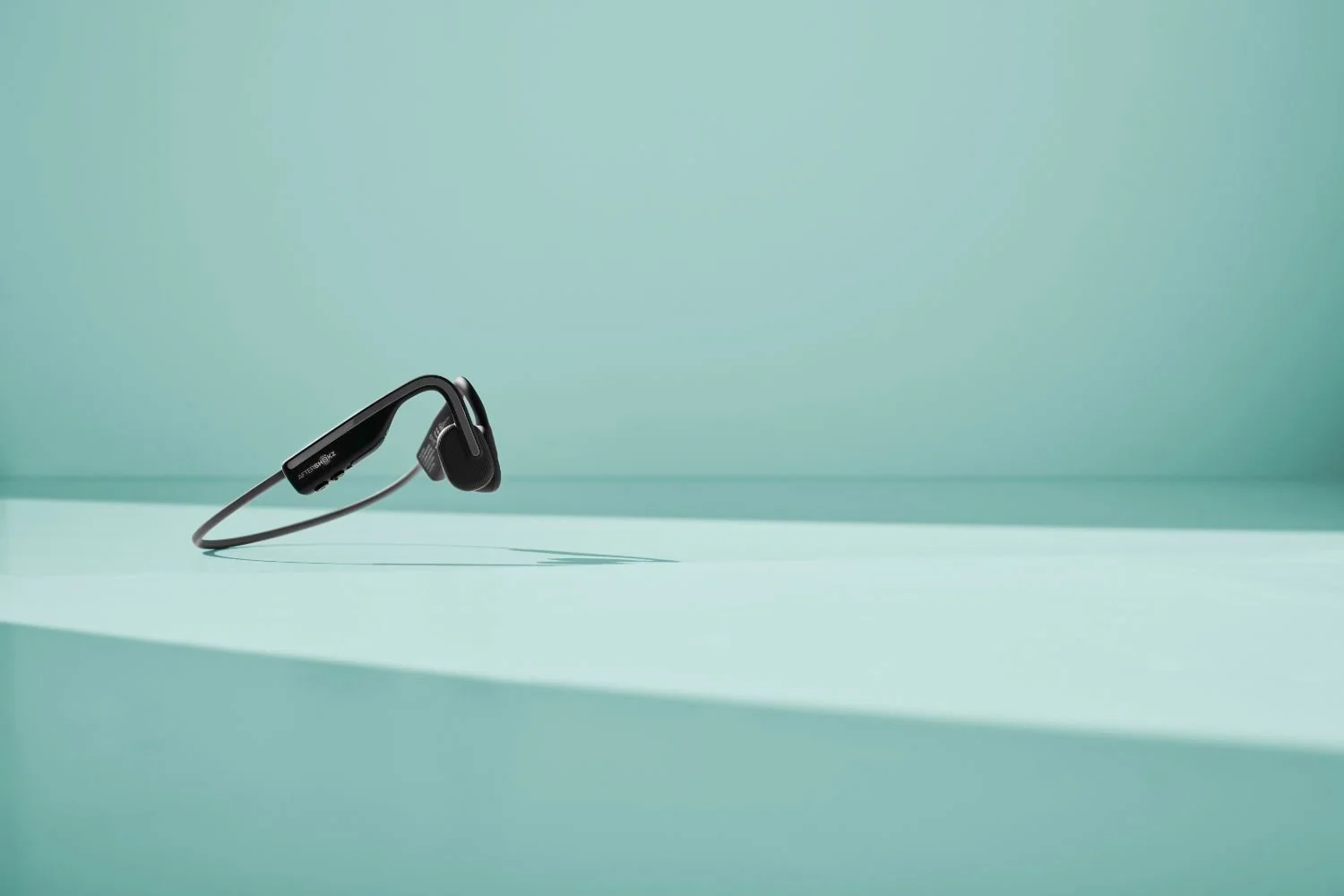 Black wireless earbud with a Bluetooth headset placed on a light teal surface against a teal background.