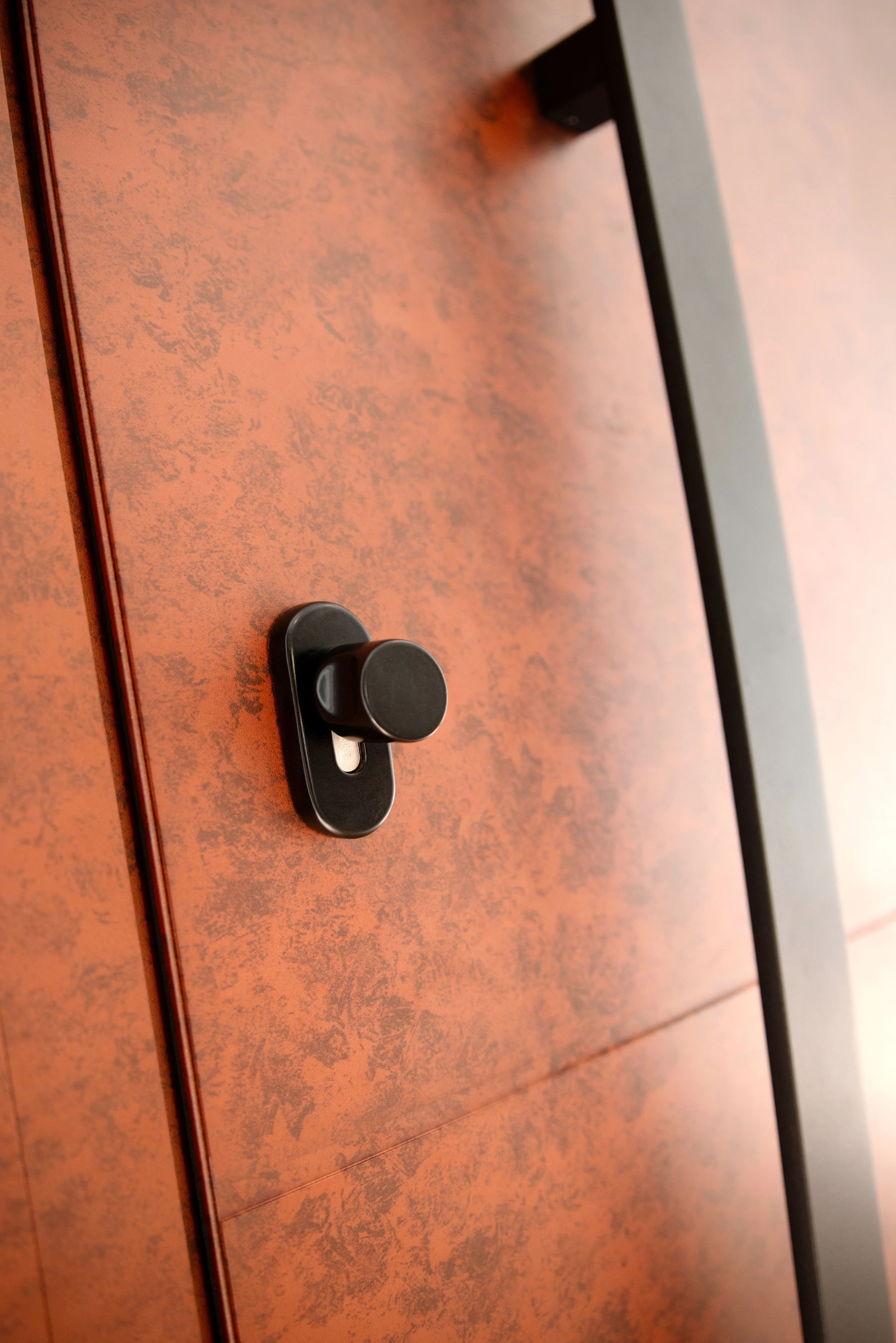 A close-up of a black electronic lock or handle on a reddish-brown textured door.