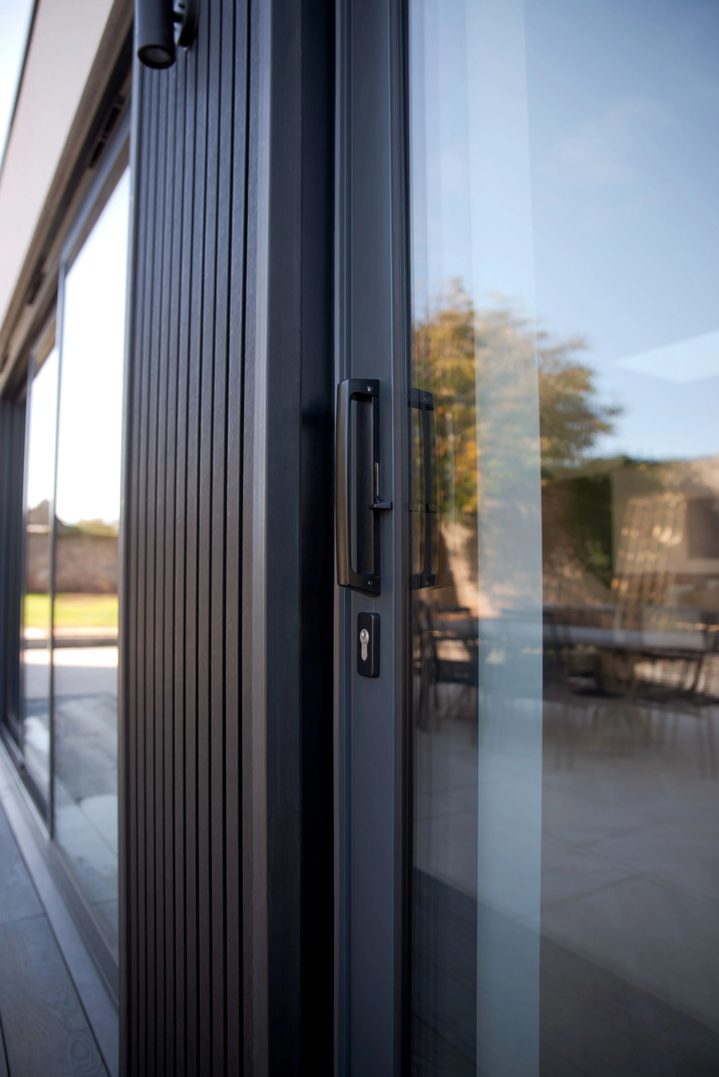 Close-up view of a sliding glass door with a black handle and lock, reflecting trees and sky outside.