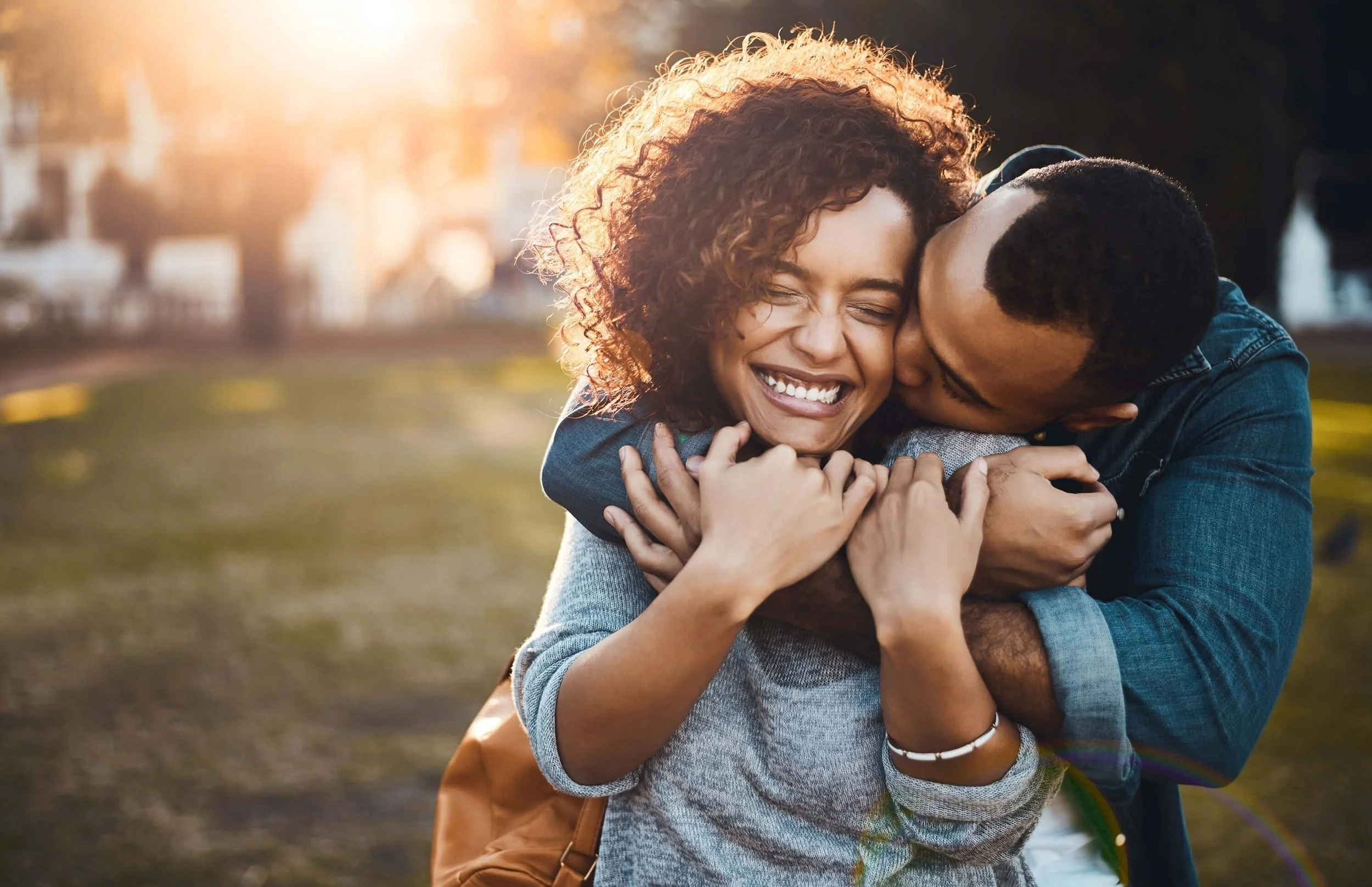 A loving couple sharing an embrace outdoors at sunset, smiling and appearing happy.