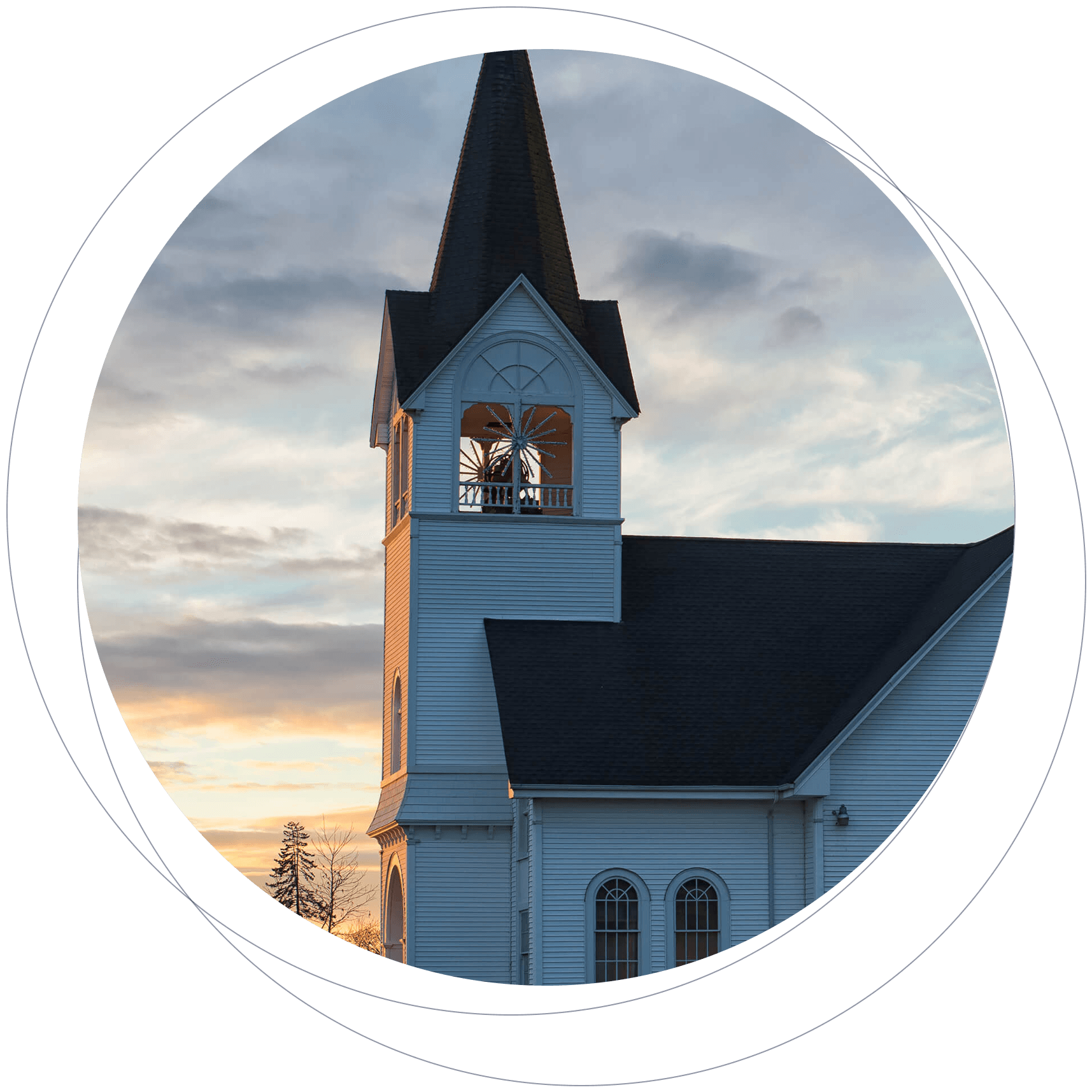 A white church with a tall steeple and clock tower at sunset, with a partly cloudy sky in the background.