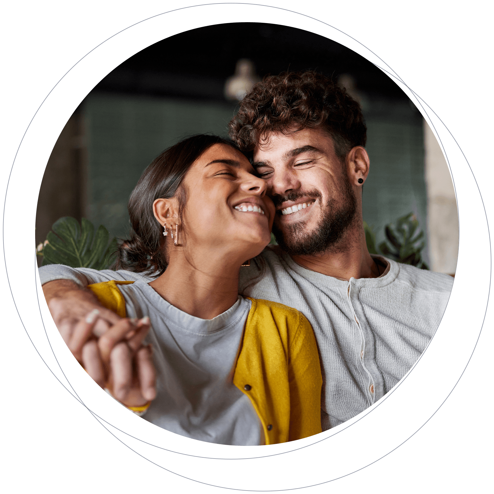 A happy couple smiling and snuggling closely together indoors with plants in the background.
