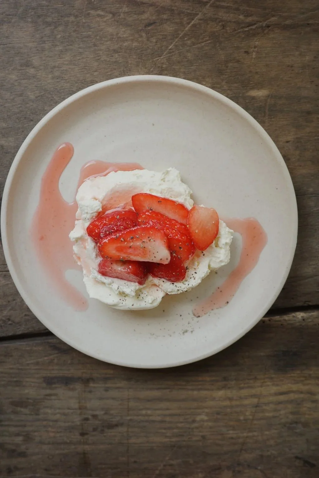 Dessert with whipped cream, sliced strawberries, strawberry sauce, and a sprinkle of black pepper on a white plate.