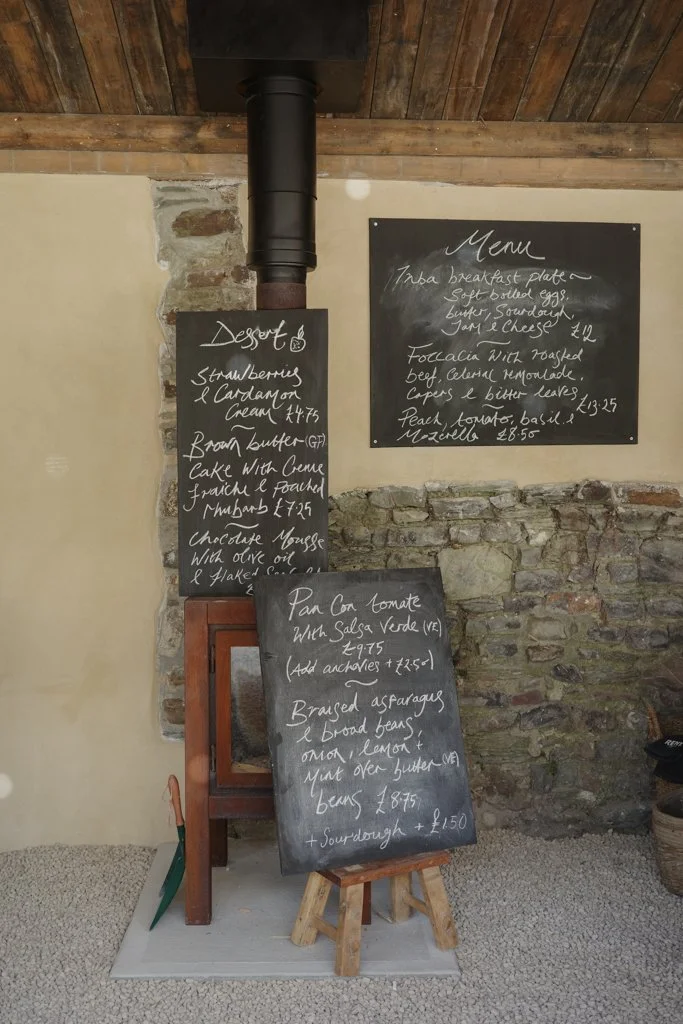 Chalkboards with handwritten menu and dessert items in a rustic setting. The menu lists breakfast and lunch options along with prices.